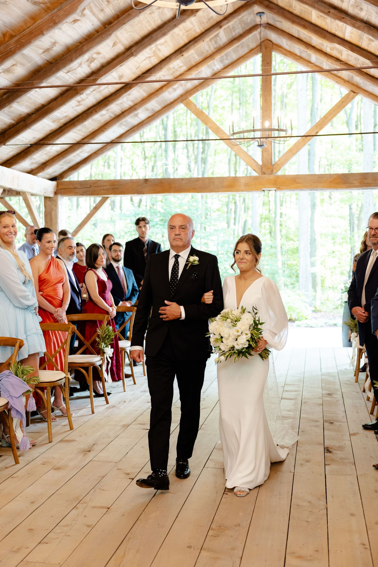 A wedding processional down a rustic wooden aisle in an elegant barn venue.