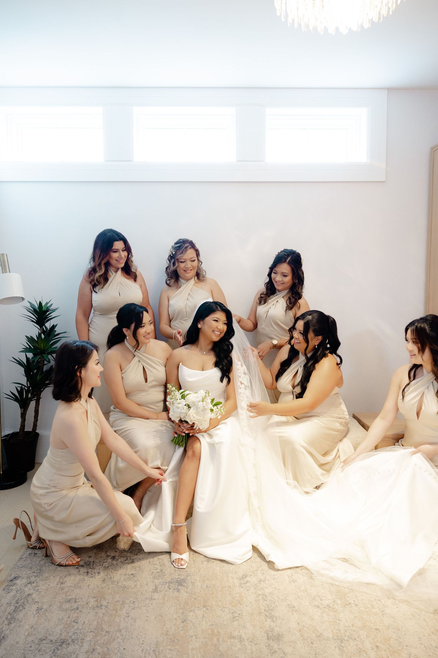 Bridal party in cream dresses gather around bride on floor sharing intimate moment.