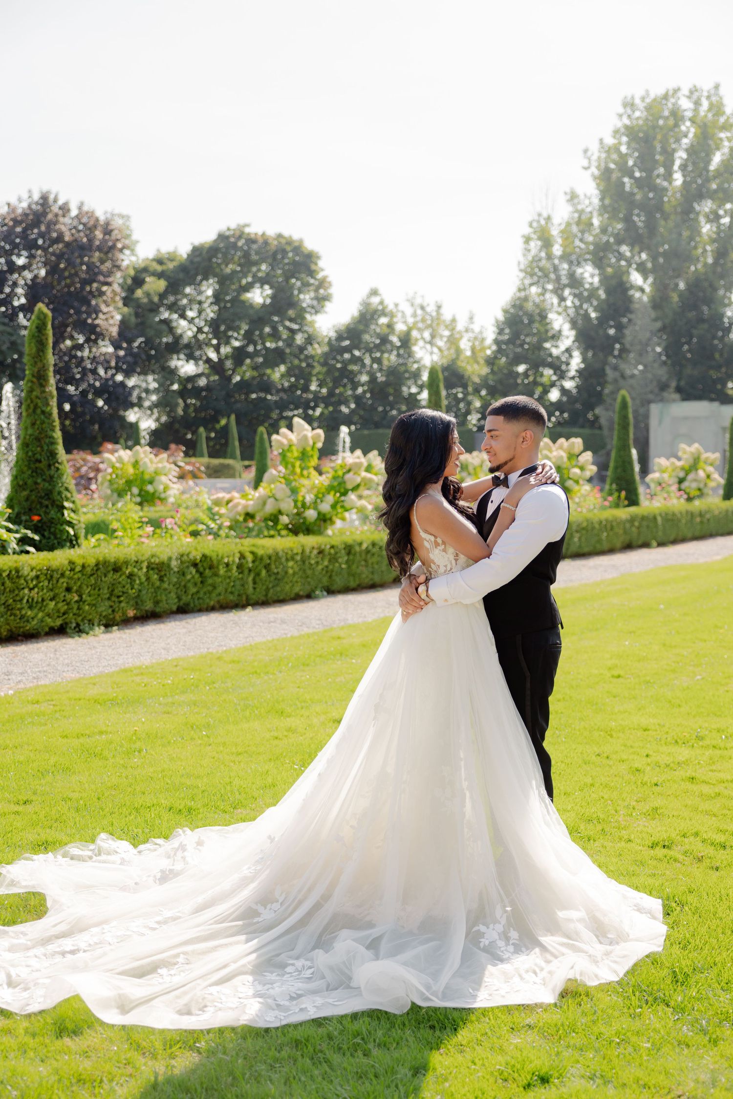 Newlyweds share a romantic pose in a formal garden with the bride's dress trailing beautifully.