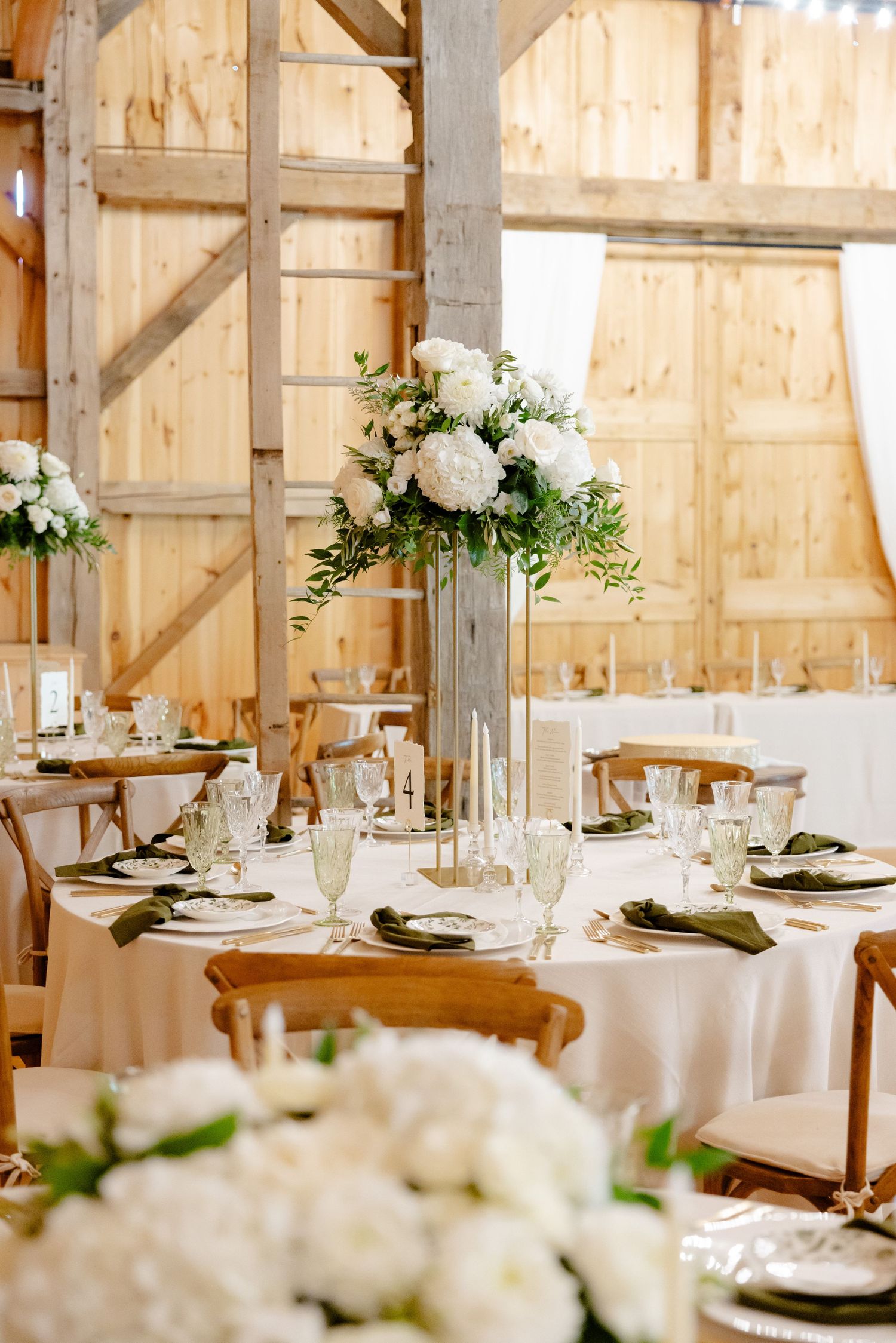Elegant wedding reception table with tall white floral centerpiece in rustic barn venue with wooden walls.