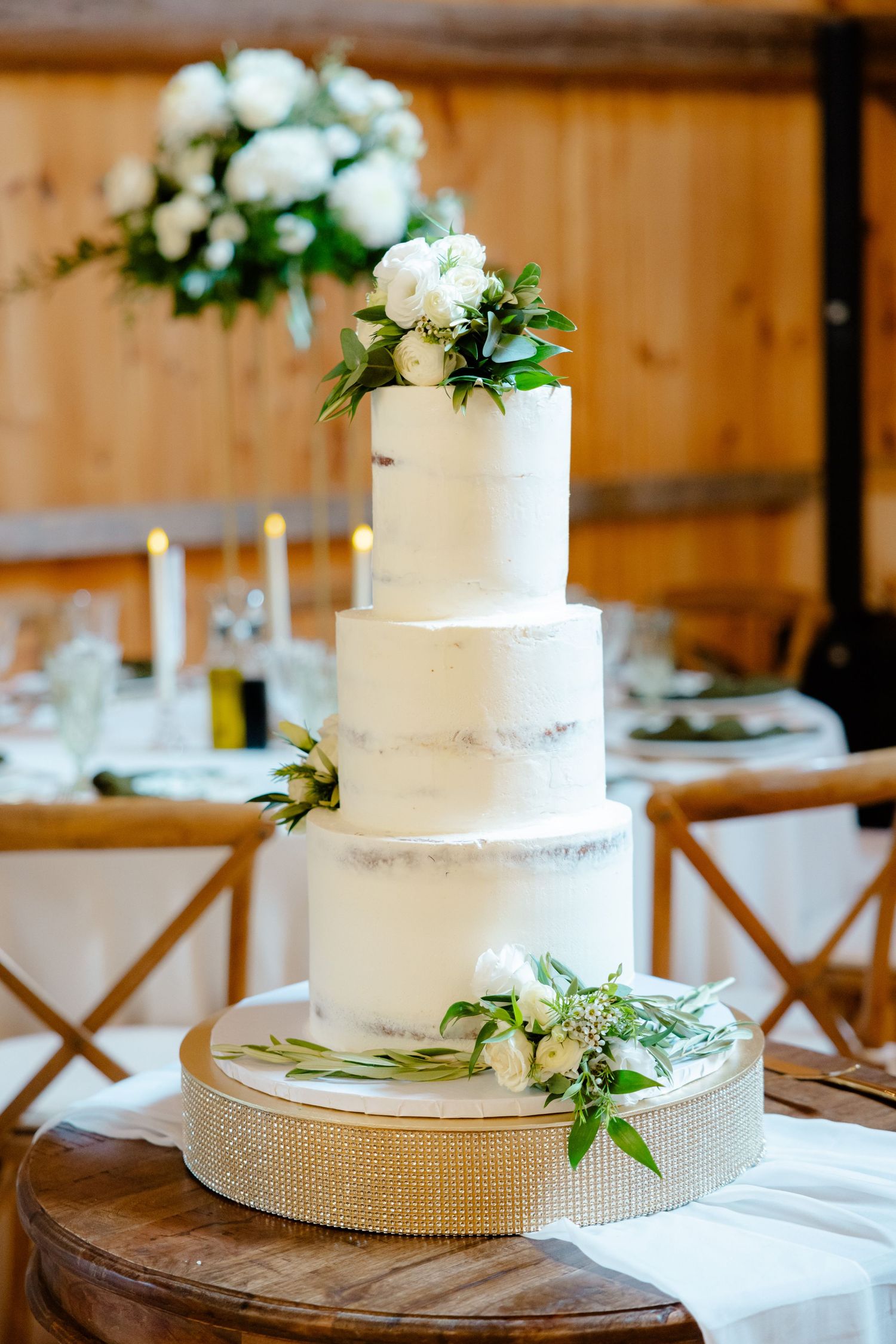 Elegant white tiered wedding cake adorned with fresh flowers and greenery on a wooden stand.