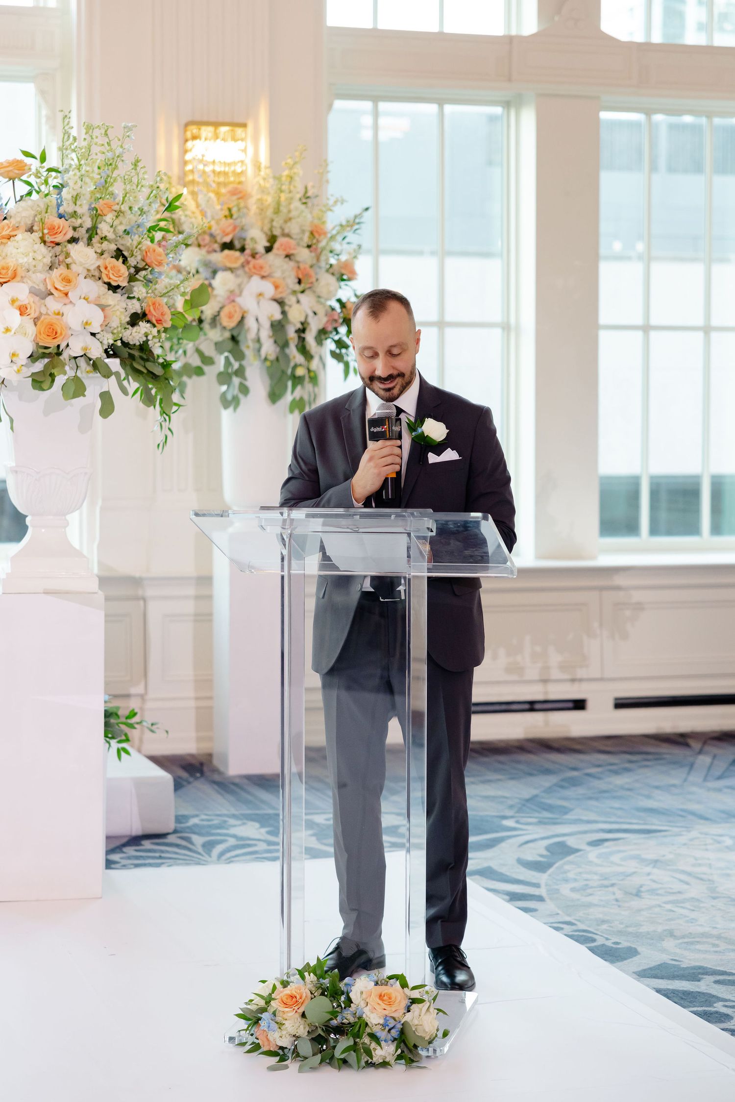 Clear acrylic podium decorated with floral arrangements at an elegant wedding venue.