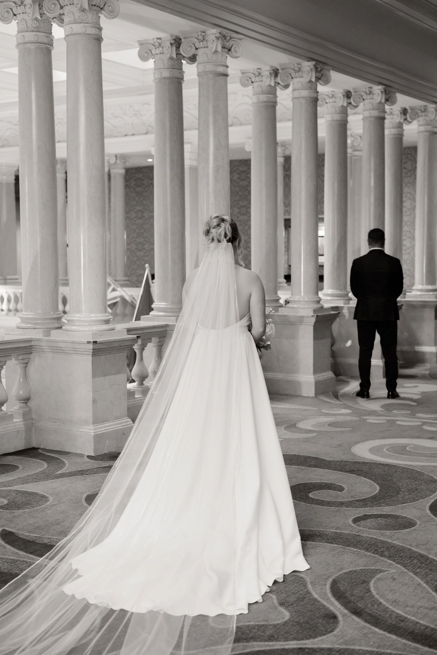 A wedding couple's silhouette against a grand colonnade with ornate floor patterns.
