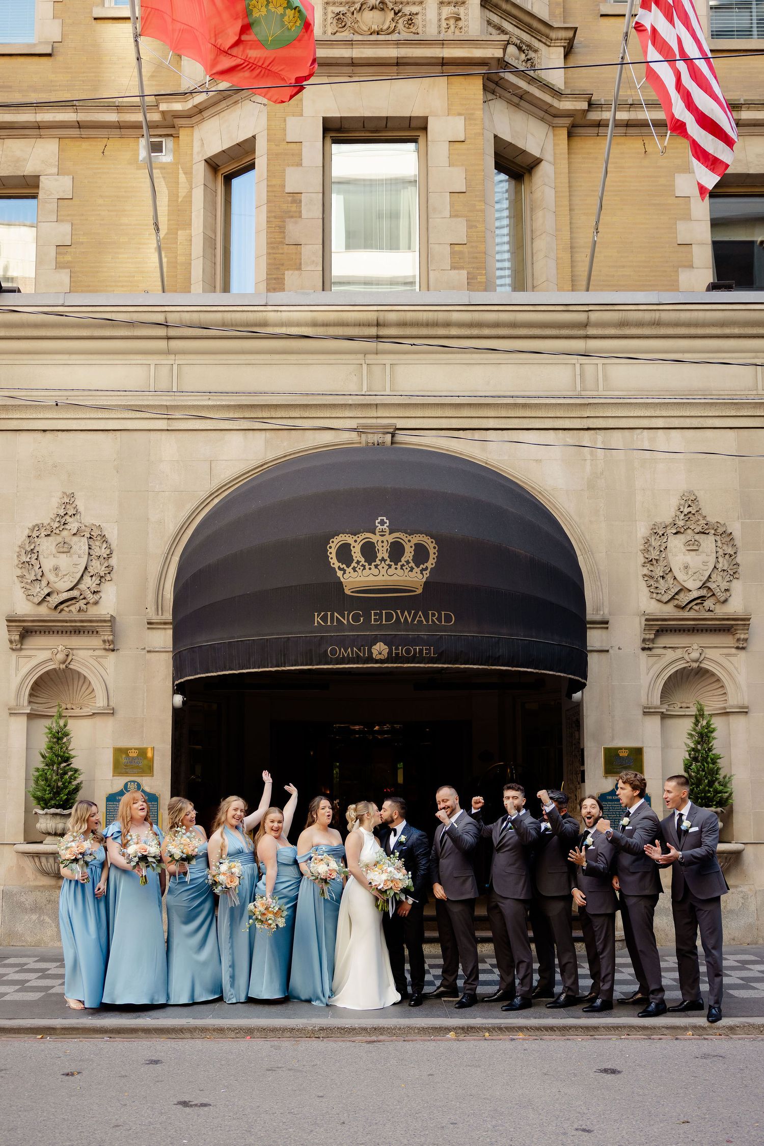 Large wedding party lined up in front of historic hotel entrance with black awnings.
