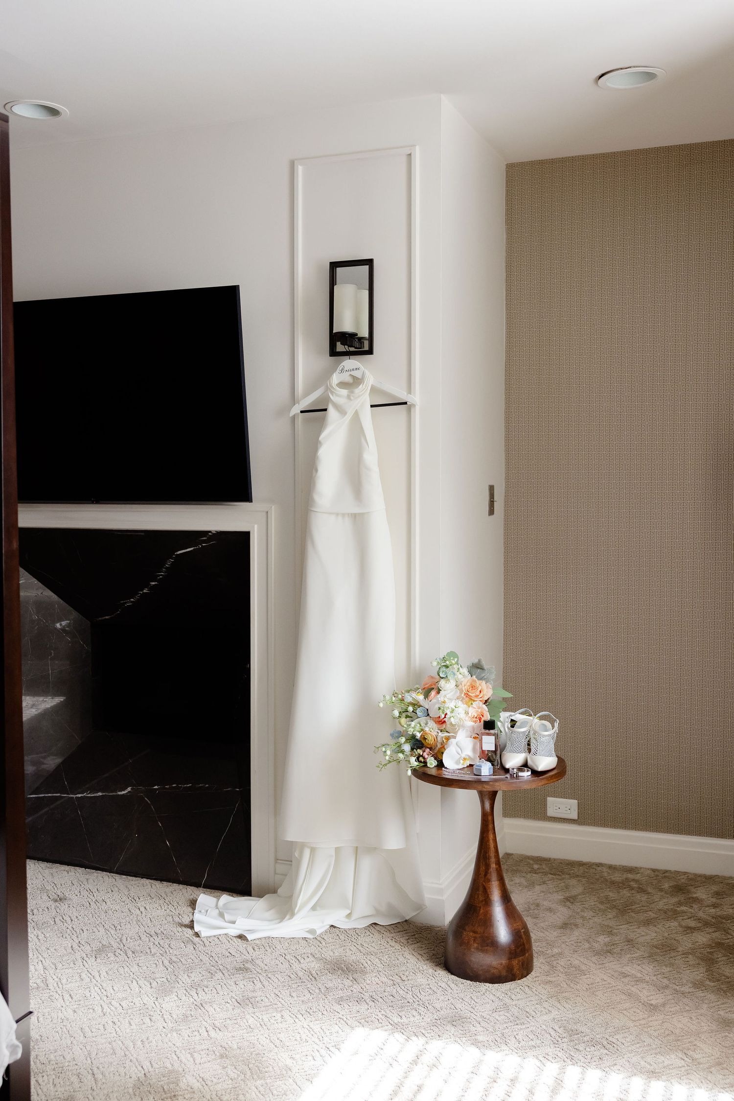 White wedding dress hanging in an elegant room with floral arrangements and natural lighting.