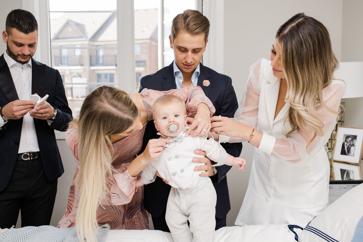 Group gathers around baby dressed in white during special occasion.