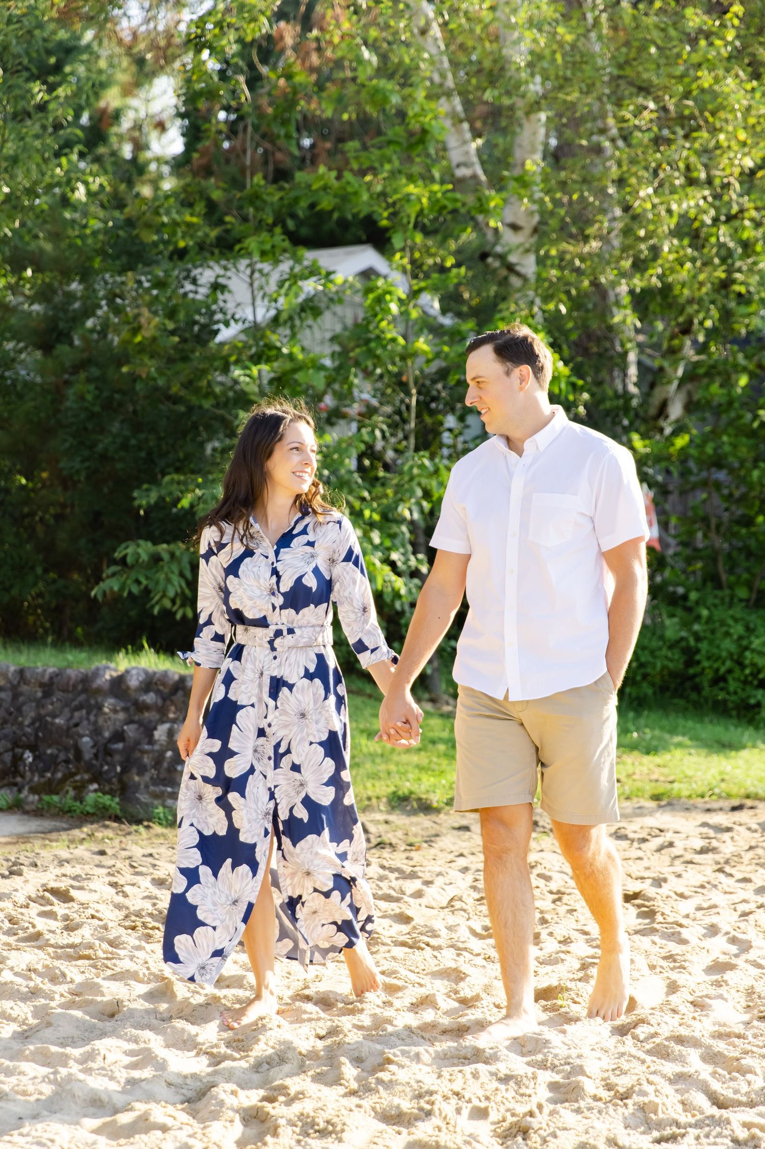 Couple holding hands while walking barefoot on sandy beach wearing coordinated summer outfits.