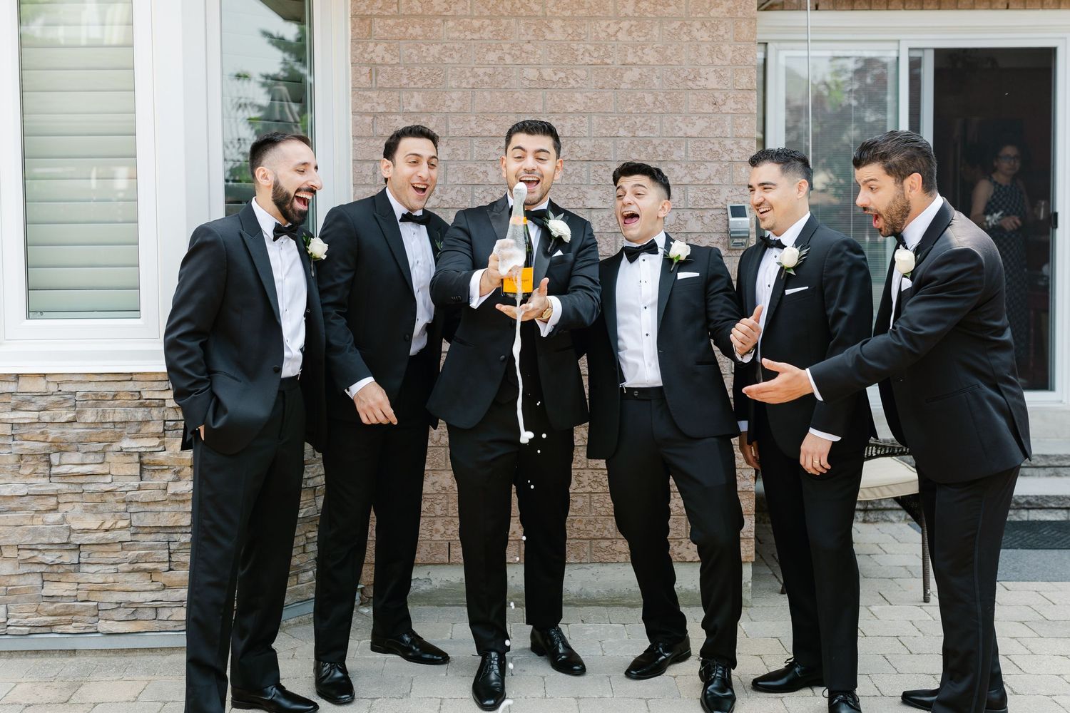 Groomsmen in black tuxedos laughing and socializing together during pre-wedding celebrations.