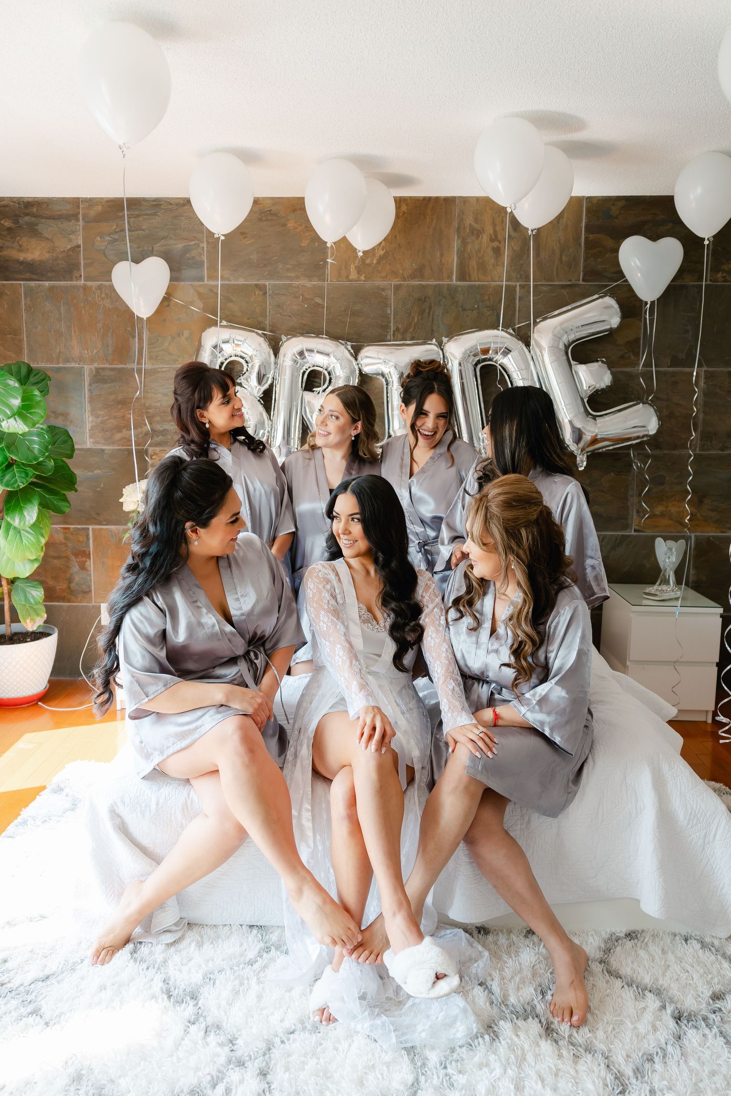 Bridesmaids in gray robes gather around the bride for a casual pre-wedding photo.