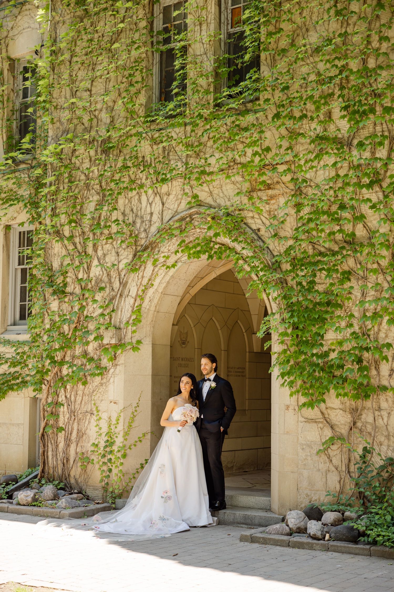 Classic wedding portrait at entrance of historic stone building with climbing ivy.