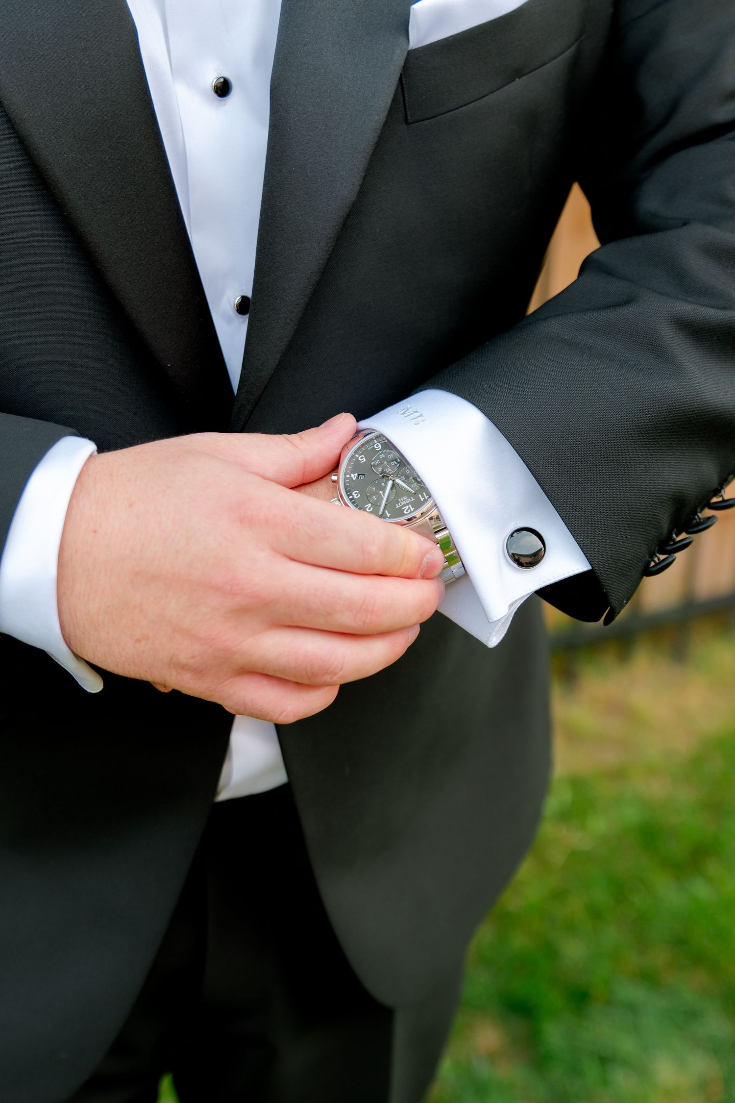 Close-up detail of tuxedo cuff links and white dress shirt at formal event.