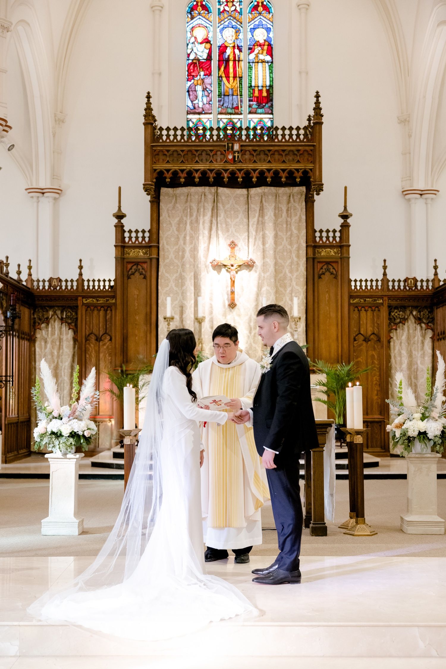A couple exchanges rings during their wedding ceremony in front of an ornate church altar.