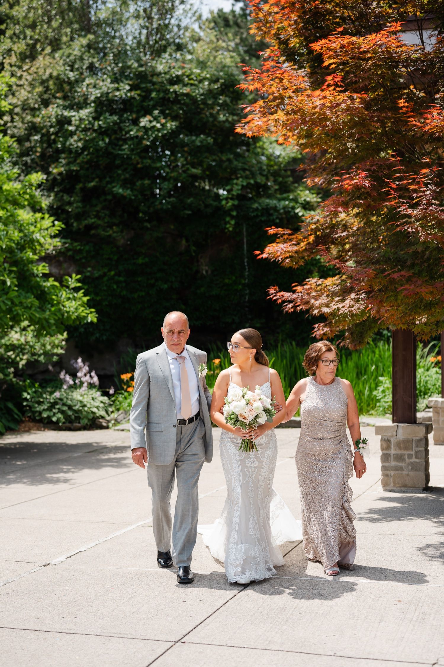 A wedding processional walking along a garden path with vibrant autumn foliage in the background.