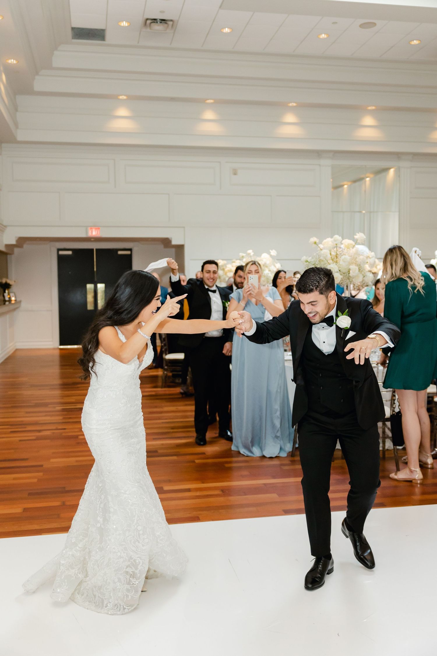 Newlyweds share their first dance at a wedding reception with guests celebrating in the background.