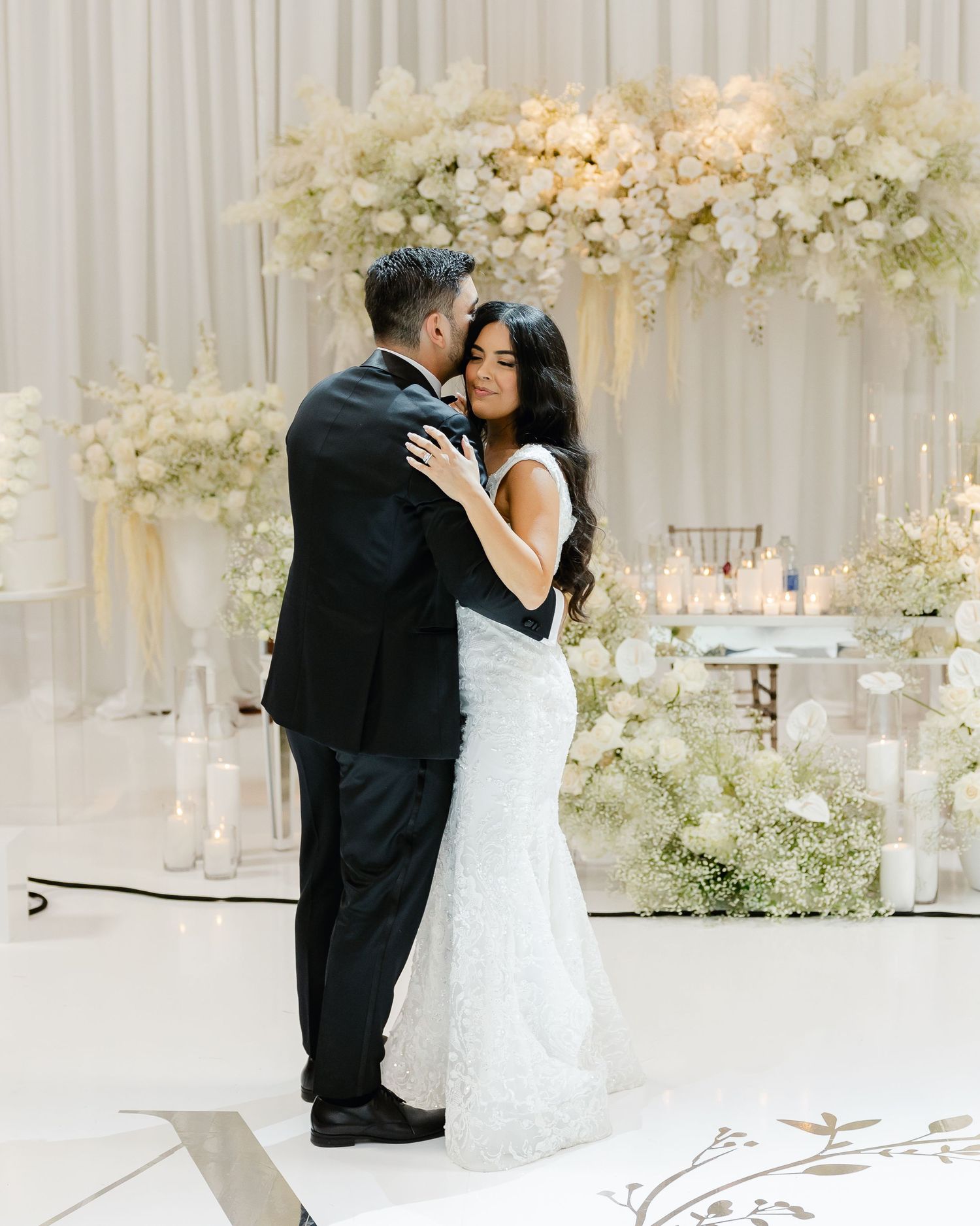 A tender embrace captured during a wedding with elegant white draping and floral decor.