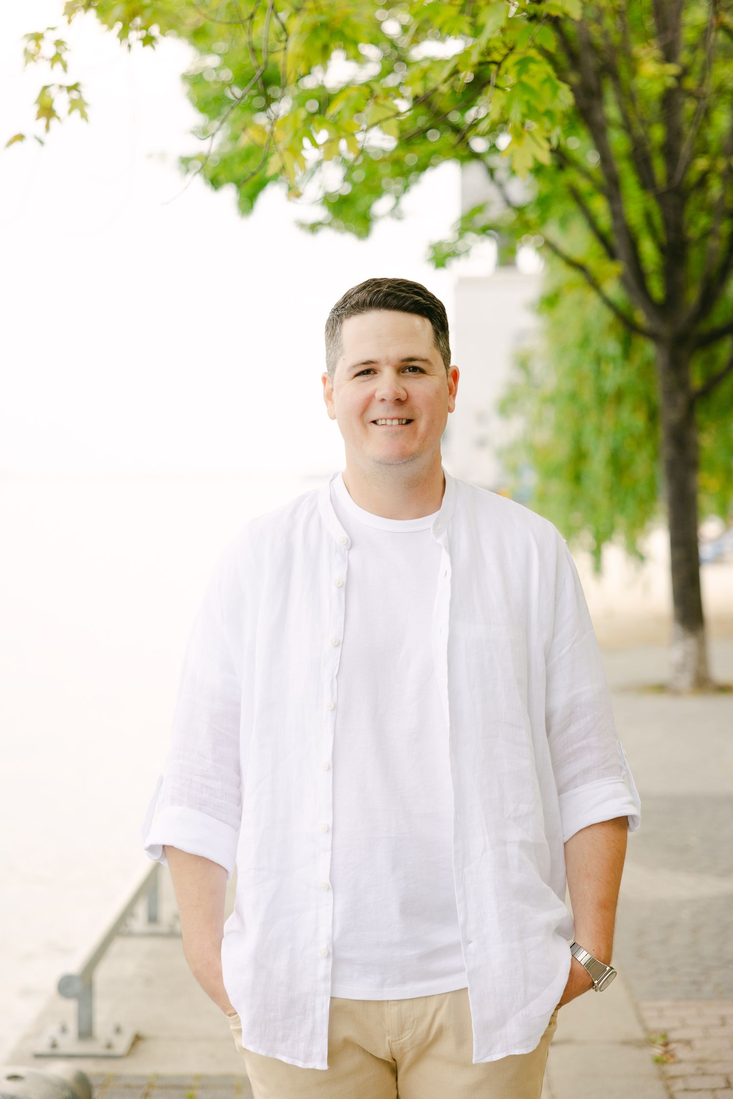Portrait of person in white button-down shirt and khaki shorts standing on waterfront path.
