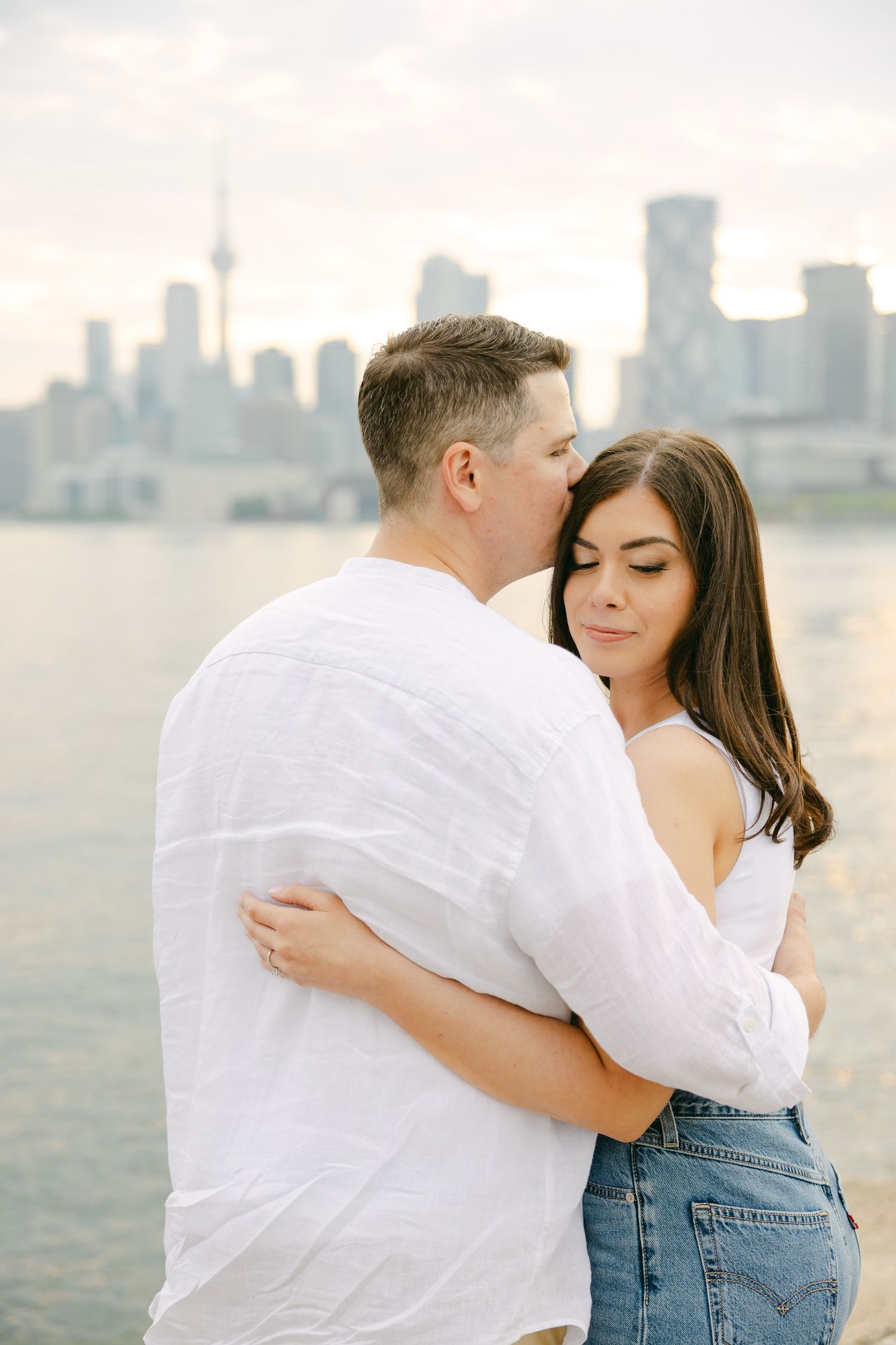 A romantic couple embraces against the Toronto skyline with the CN Tower visible in the background.