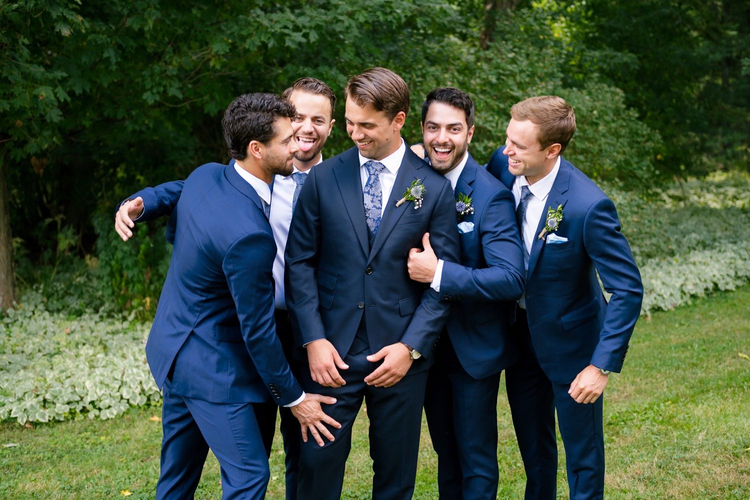 Groomsmen laughing and joking together during outdoor wedding photo session.