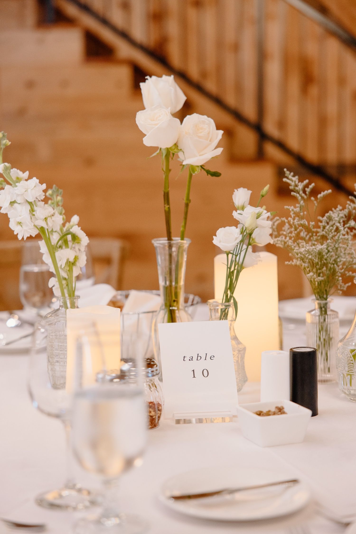 Minimalist table setting with white roses, candlelight, and table number at wedding reception.