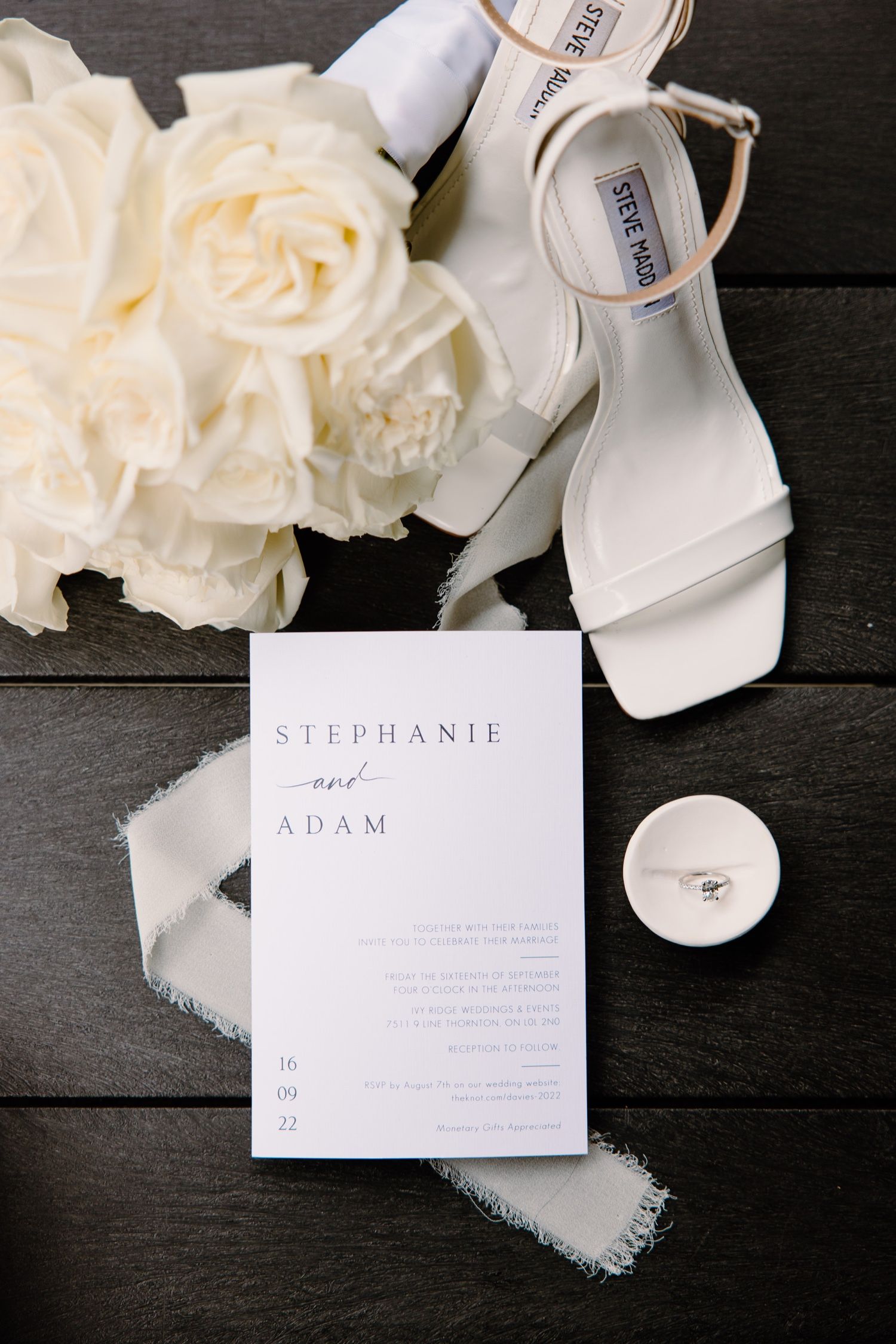 White bridal shoes and roses displayed with a wedding invitation for Stephanie and Adam.