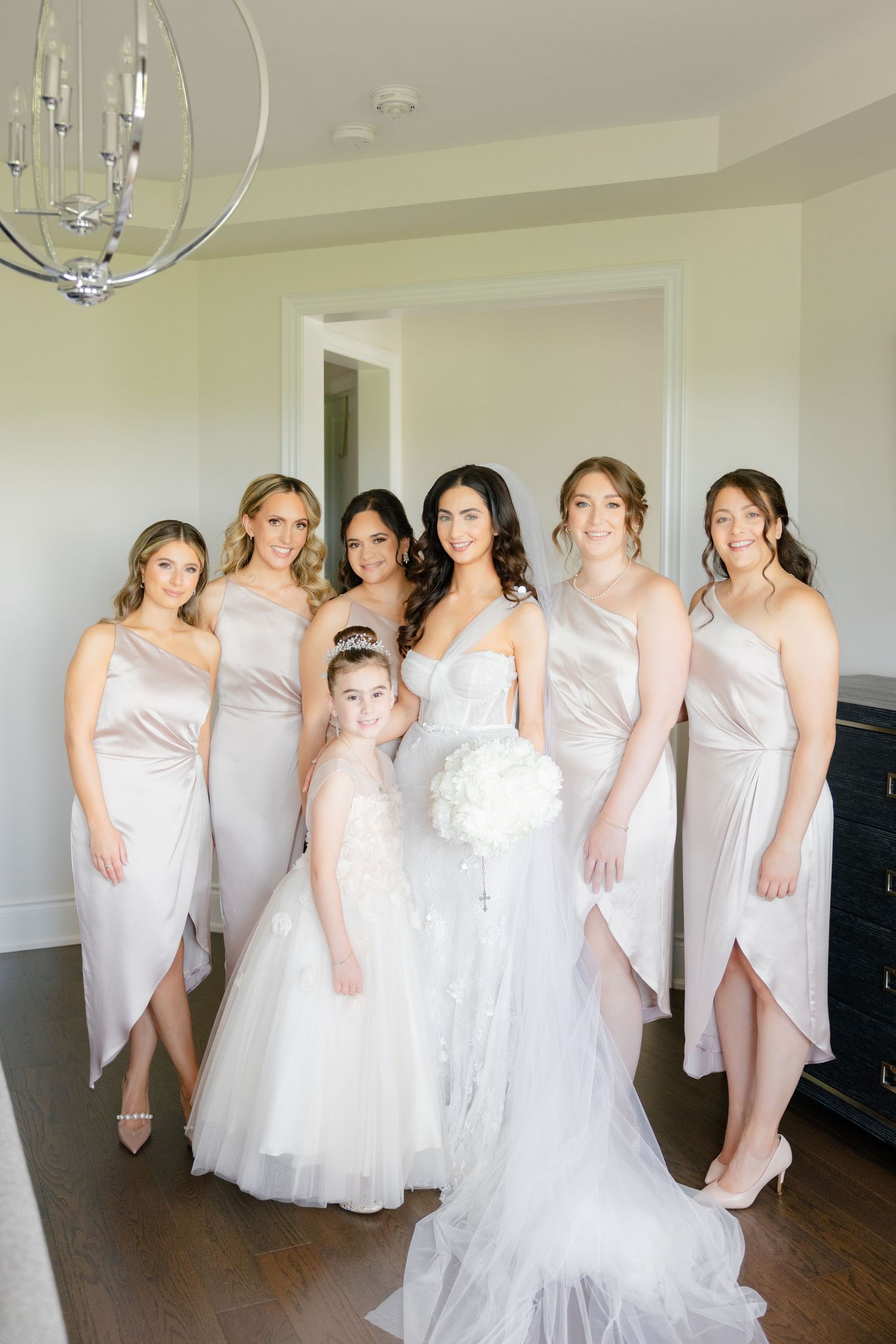 Bridesmaids in champagne dresses surround a bride in white for a formal wedding portrait.