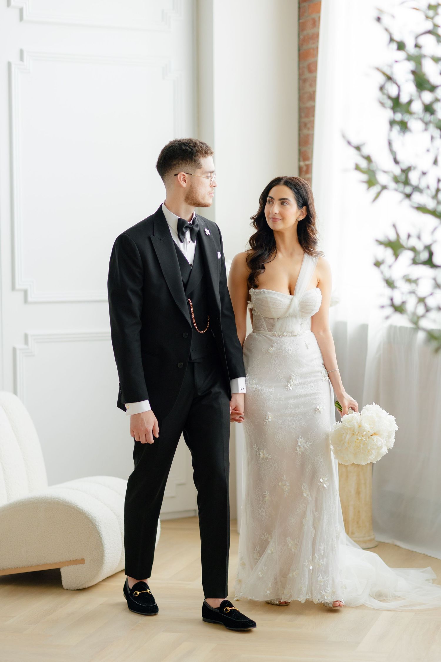Wedding couple poses in a minimalist white room with floor-to-ceiling windows and modern decor.