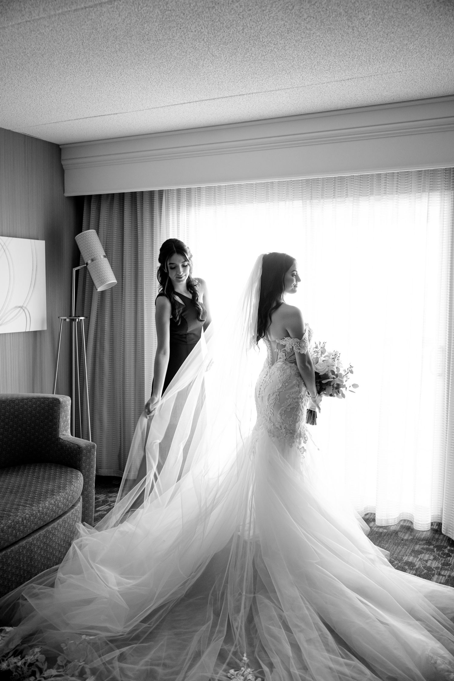 Dramatic black and white bridal portrait with flowing veil by a sunlit window.