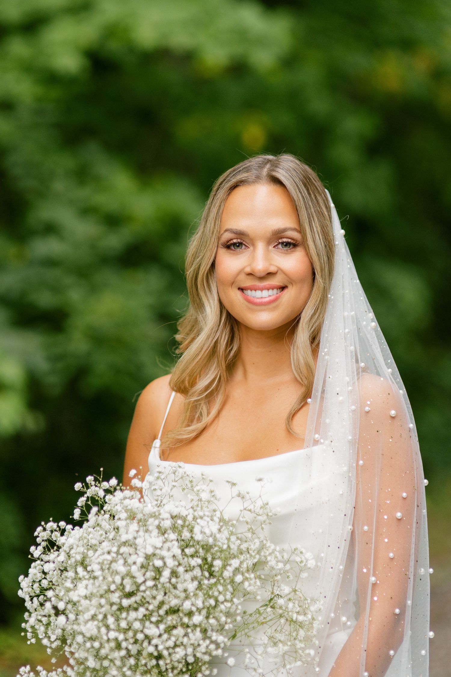 Close up bridal portrait with delicate pearl veil and baby's breath bouquet.