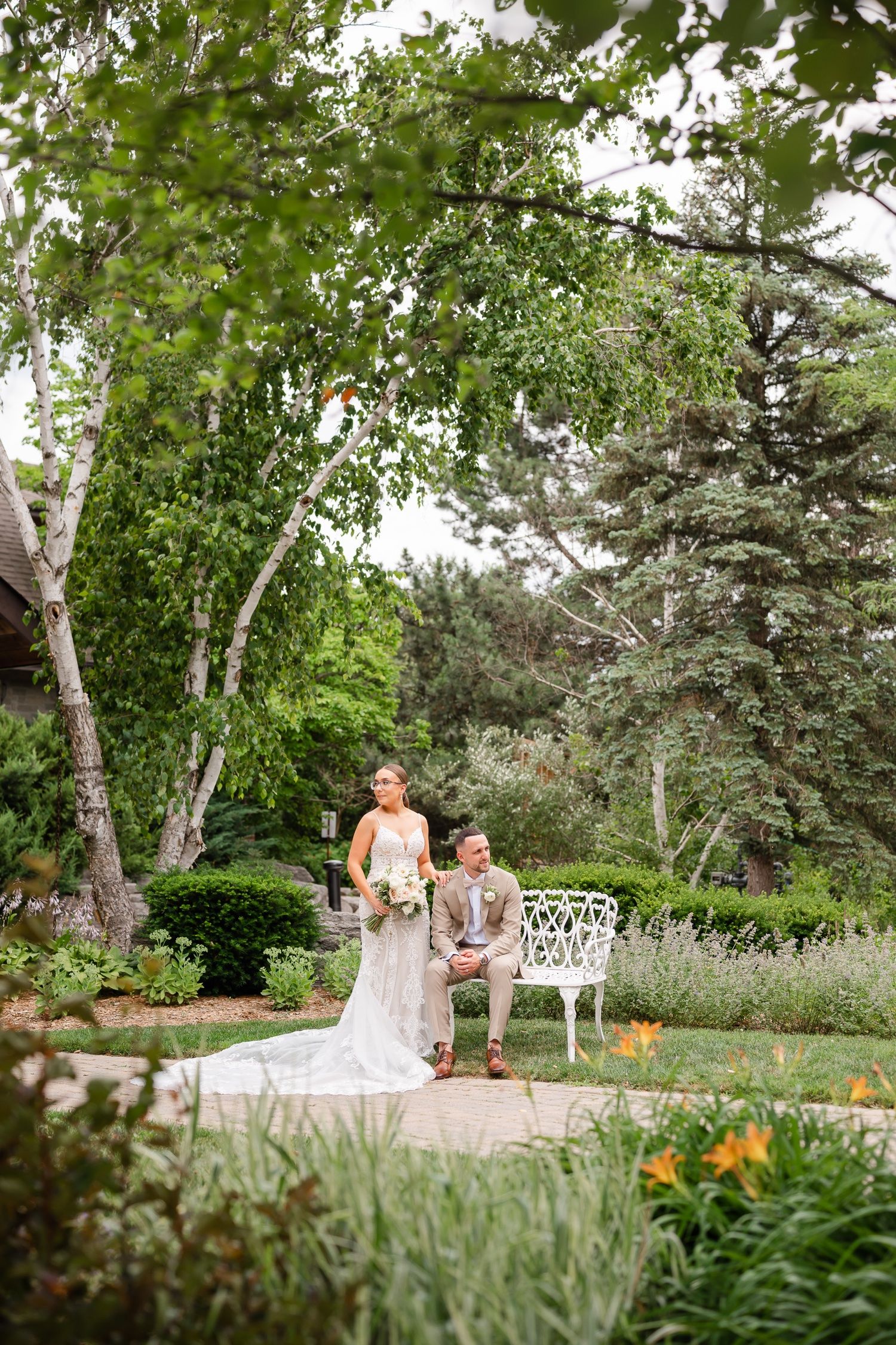 A wedding photo in a lush garden setting with birch trees and evergreens creating a natural backdrop.