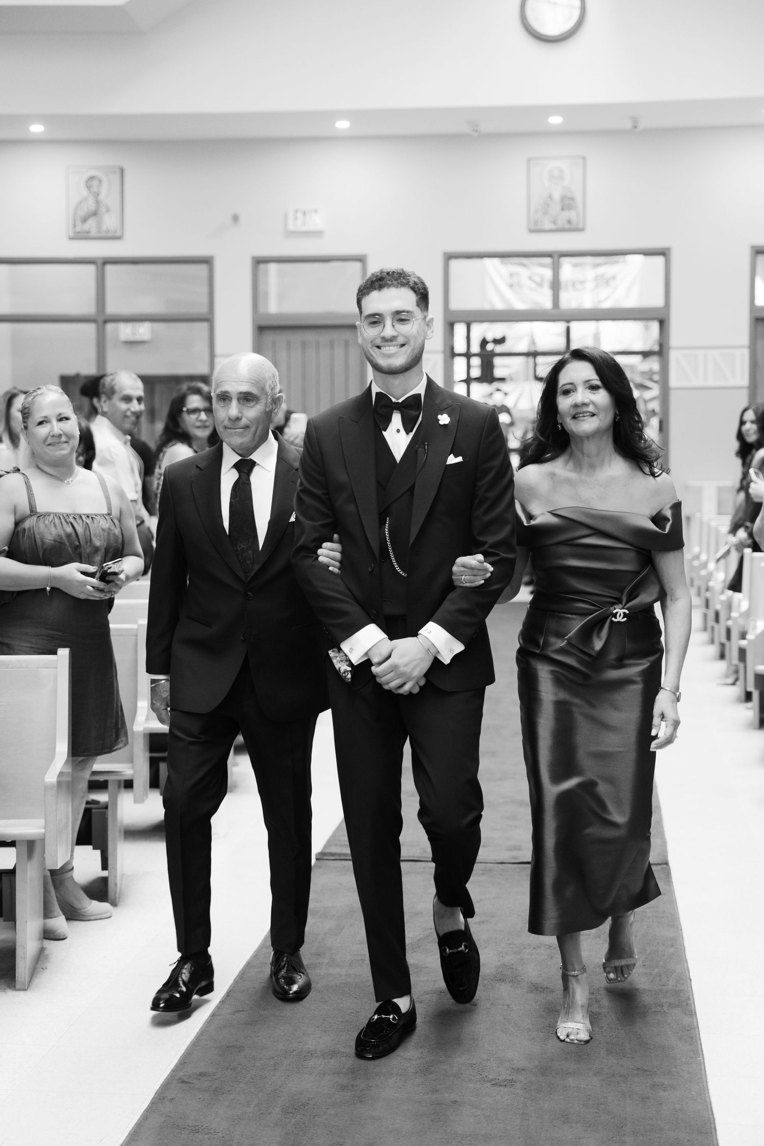 Black and white photo of wedding party members walking down church aisle during ceremony.
