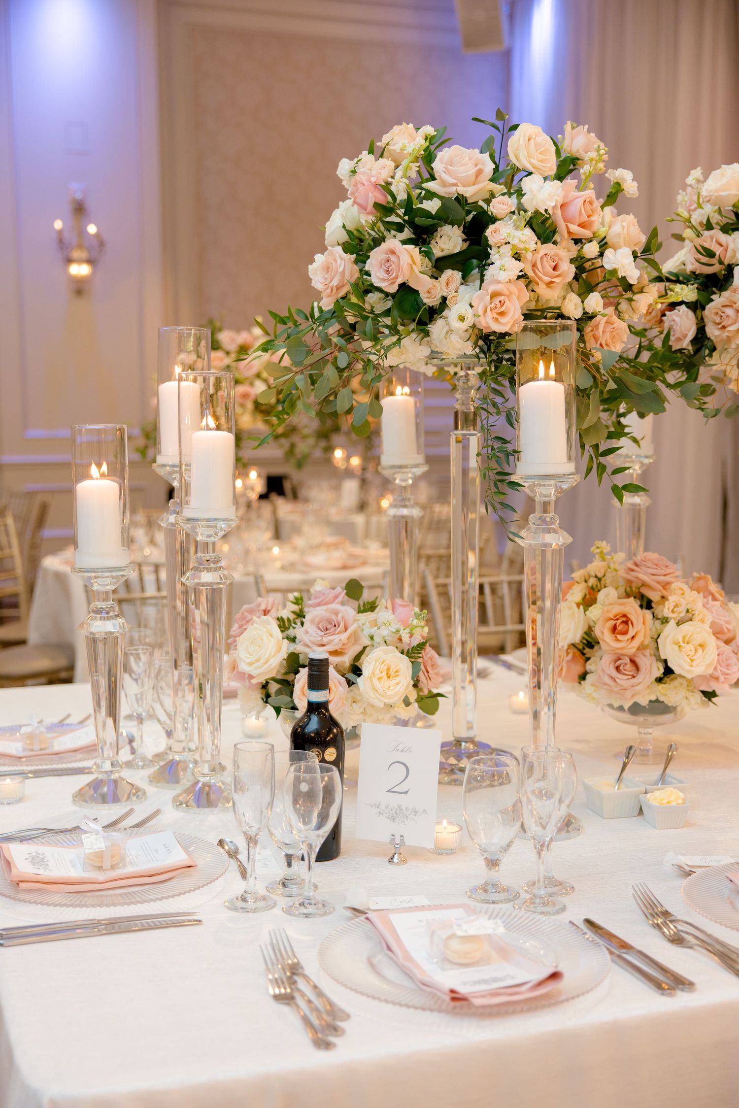 Luxurious wedding reception table setting with tall floral centerpieces and glowing candles.