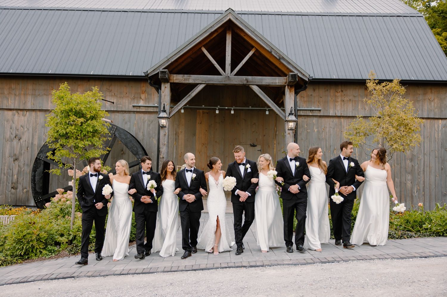Candid wedding party photo showing group walking and laughing outside rustic barn venue.