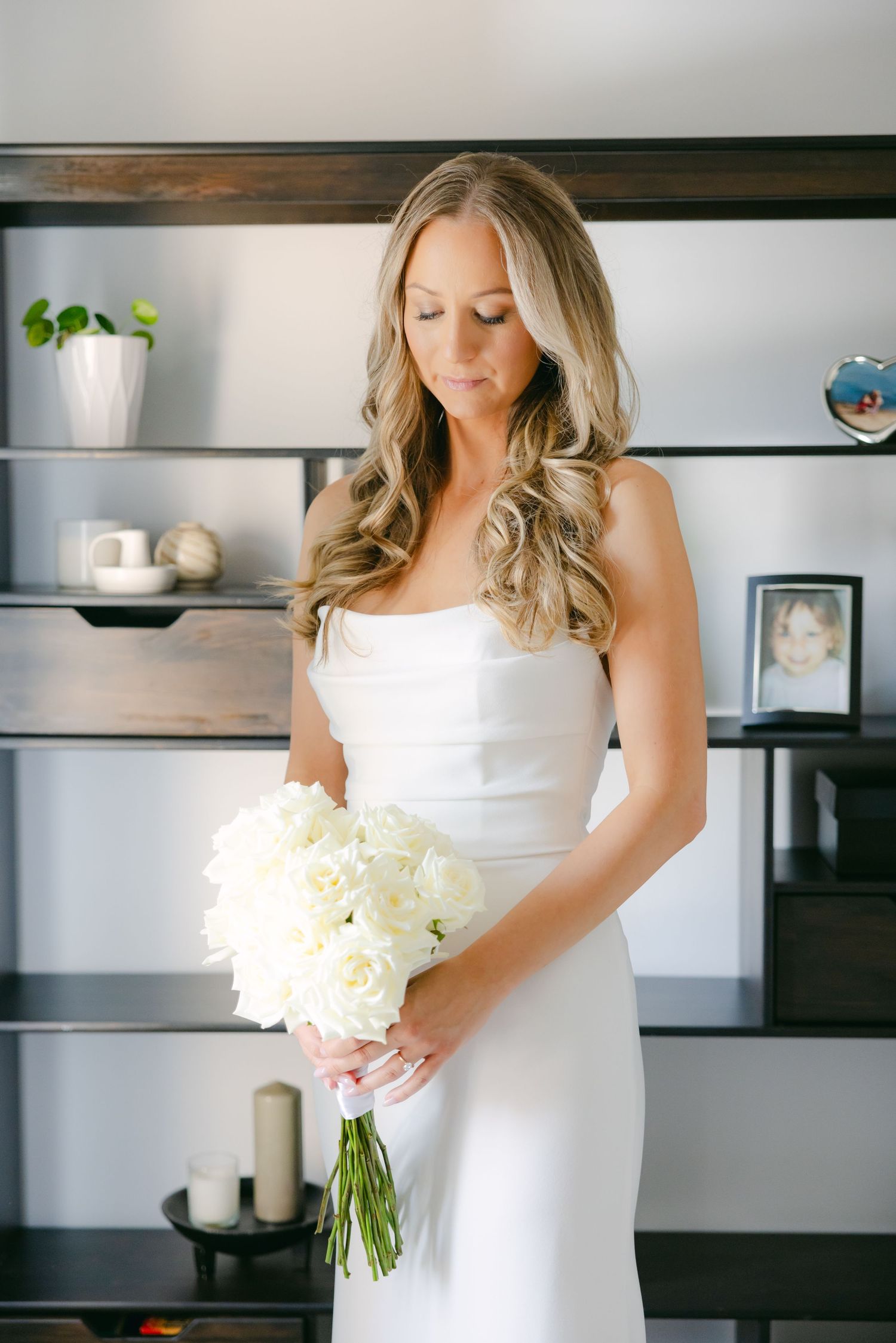 Elegant bride holding white peony bouquet against modern shelving background.