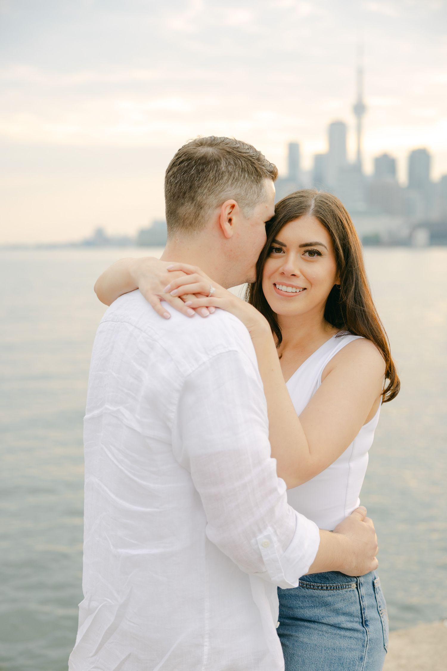 Tender embrace on waterfront with CN Tower and Toronto skyline in background.