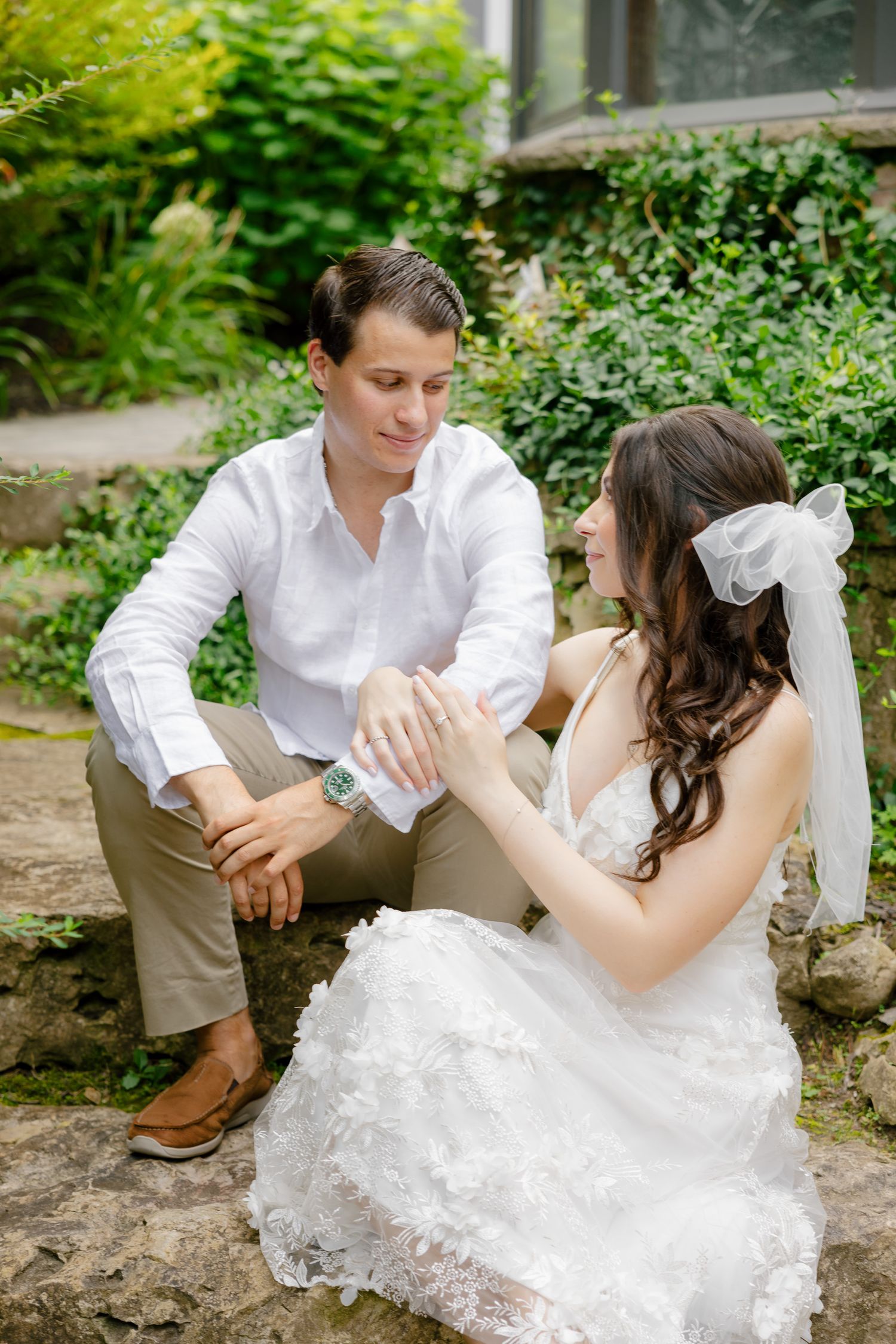 A couple sits together on stone steps in a garden surrounded by greenery.