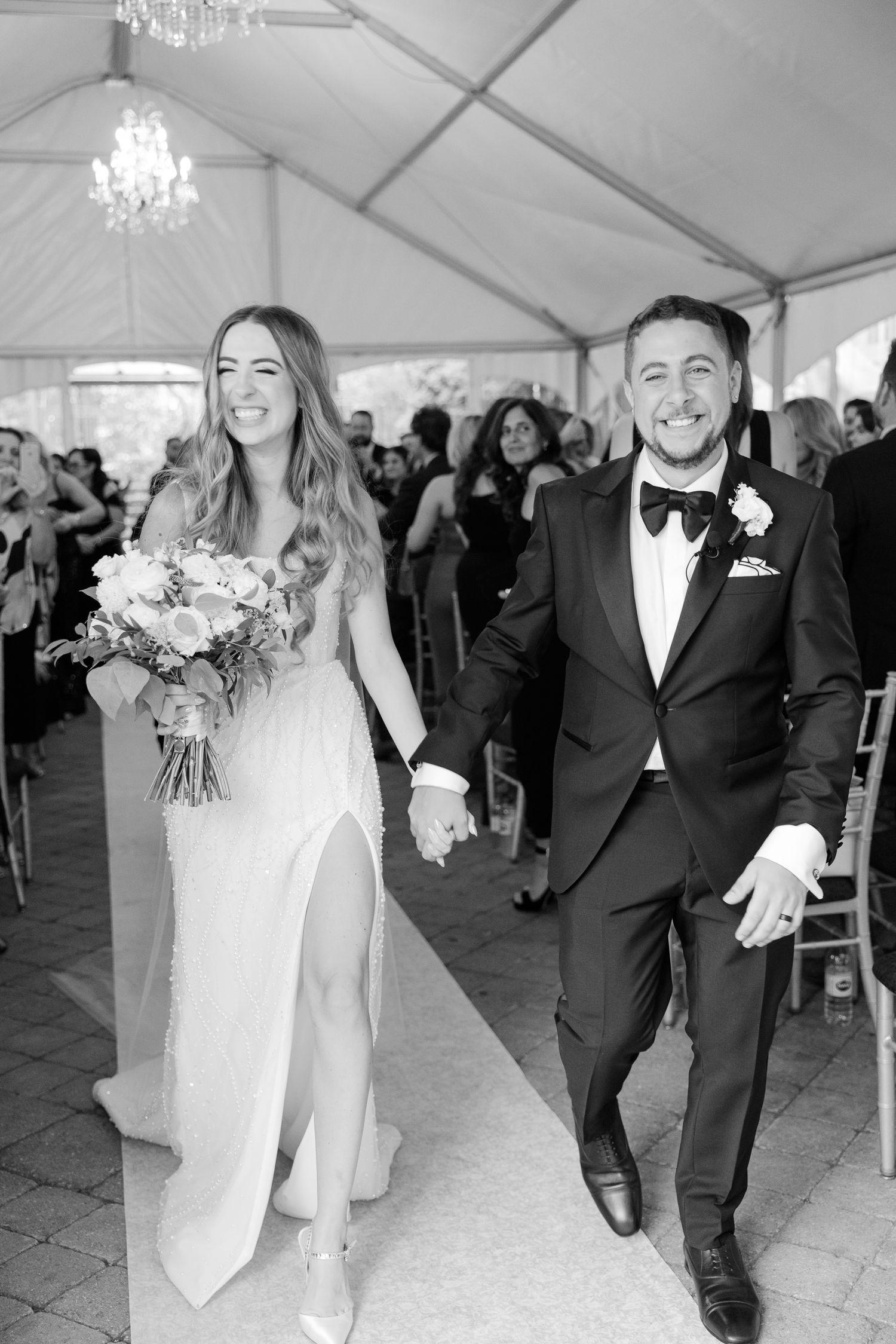 Black and white photo of a newlywed couple walking down the aisle while holding hands and smiling.