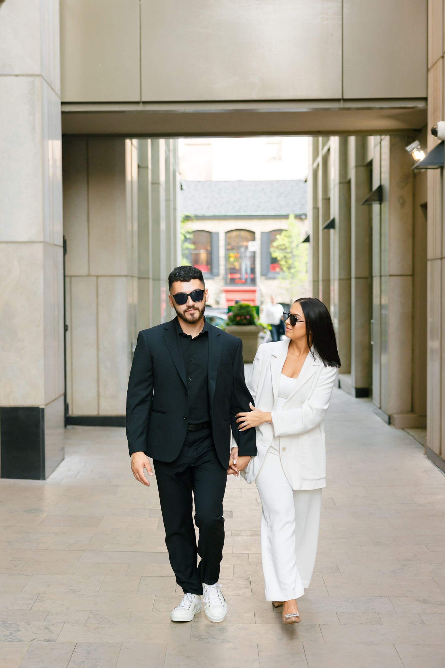 Couple in contrasting black and white outfits walking through an urban corridor.