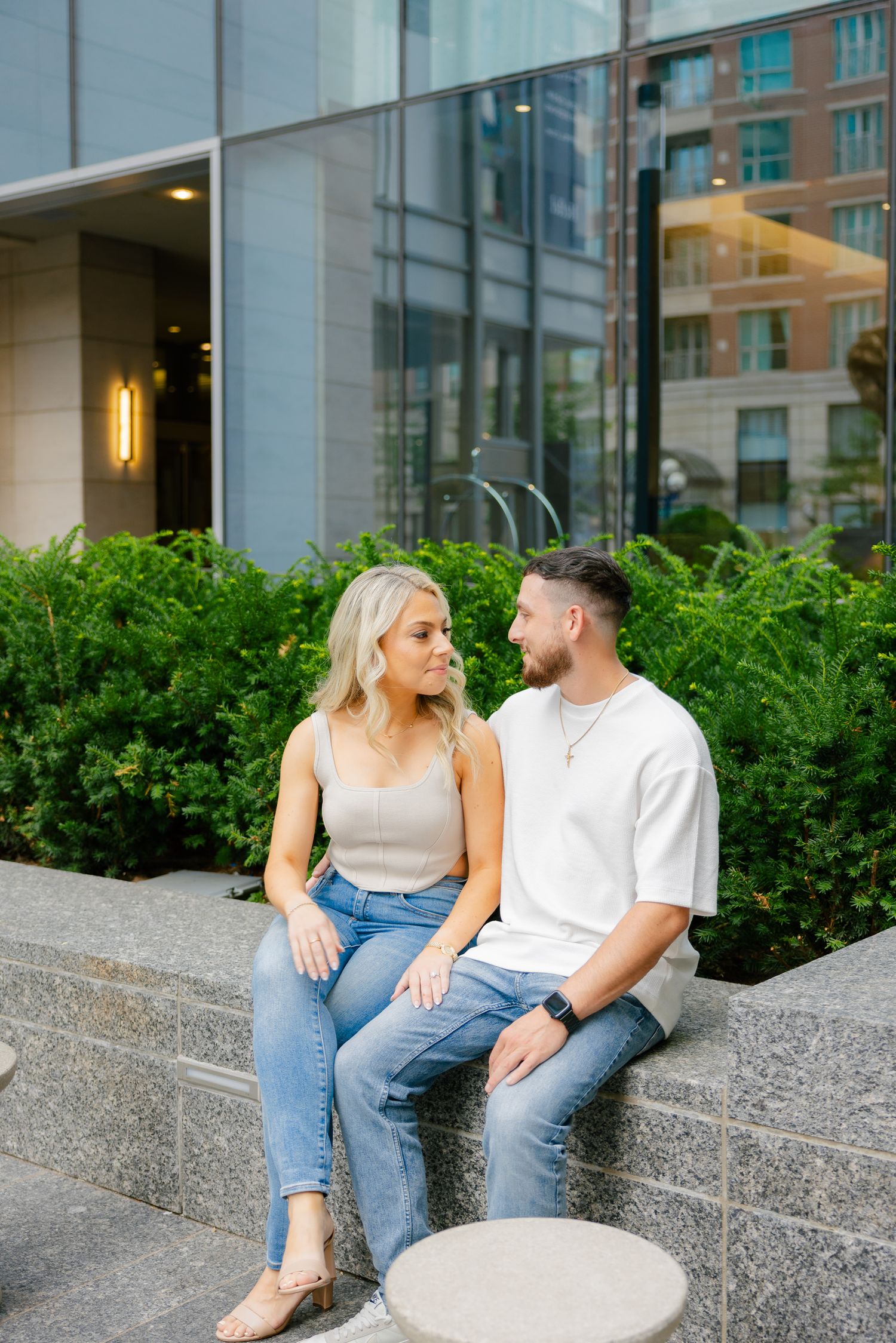 A couple sitting together on stone steps with modern architecture and greenery in background.