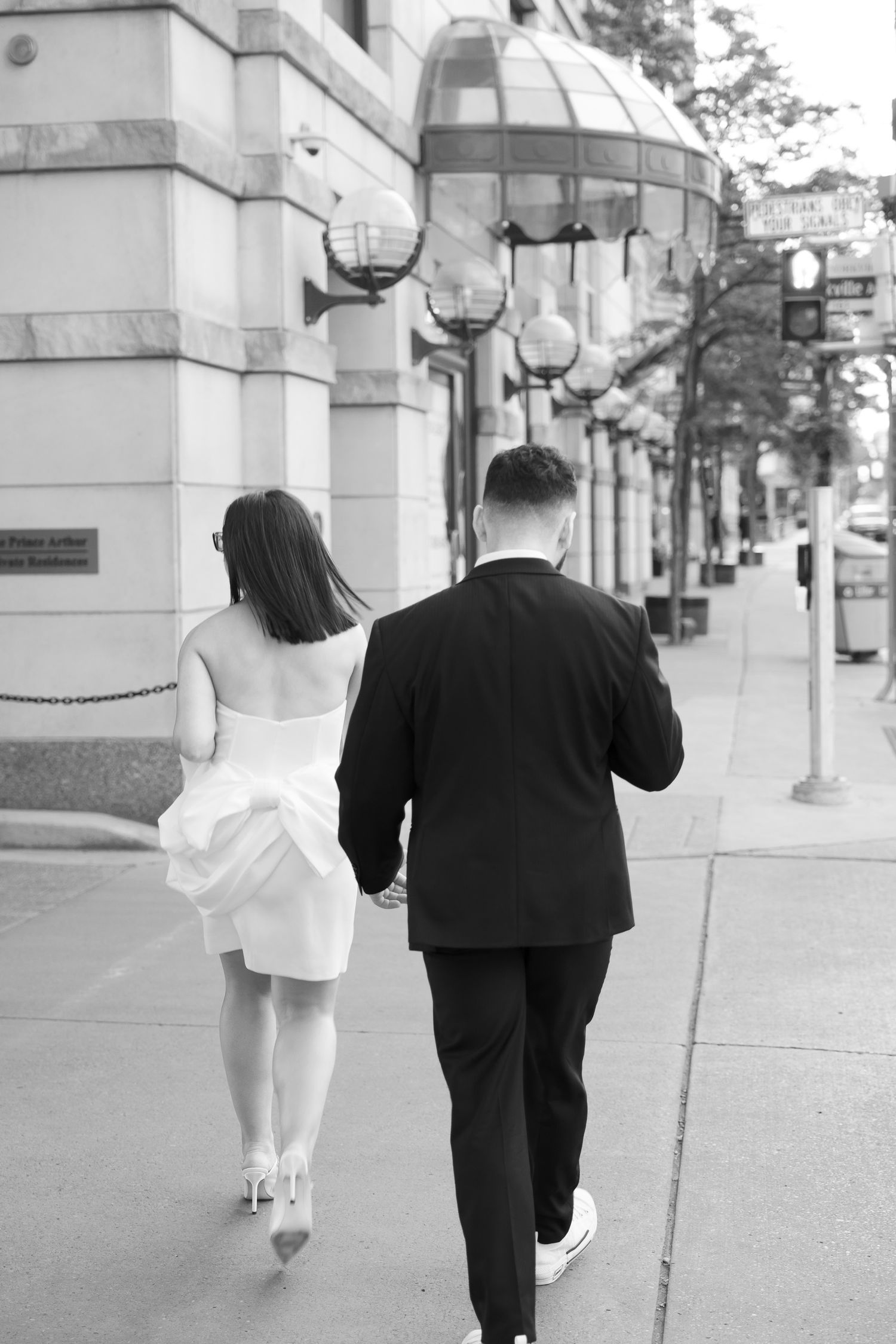 Black and white photo of a couple walking down a city sidewalk with decorative street lamps.