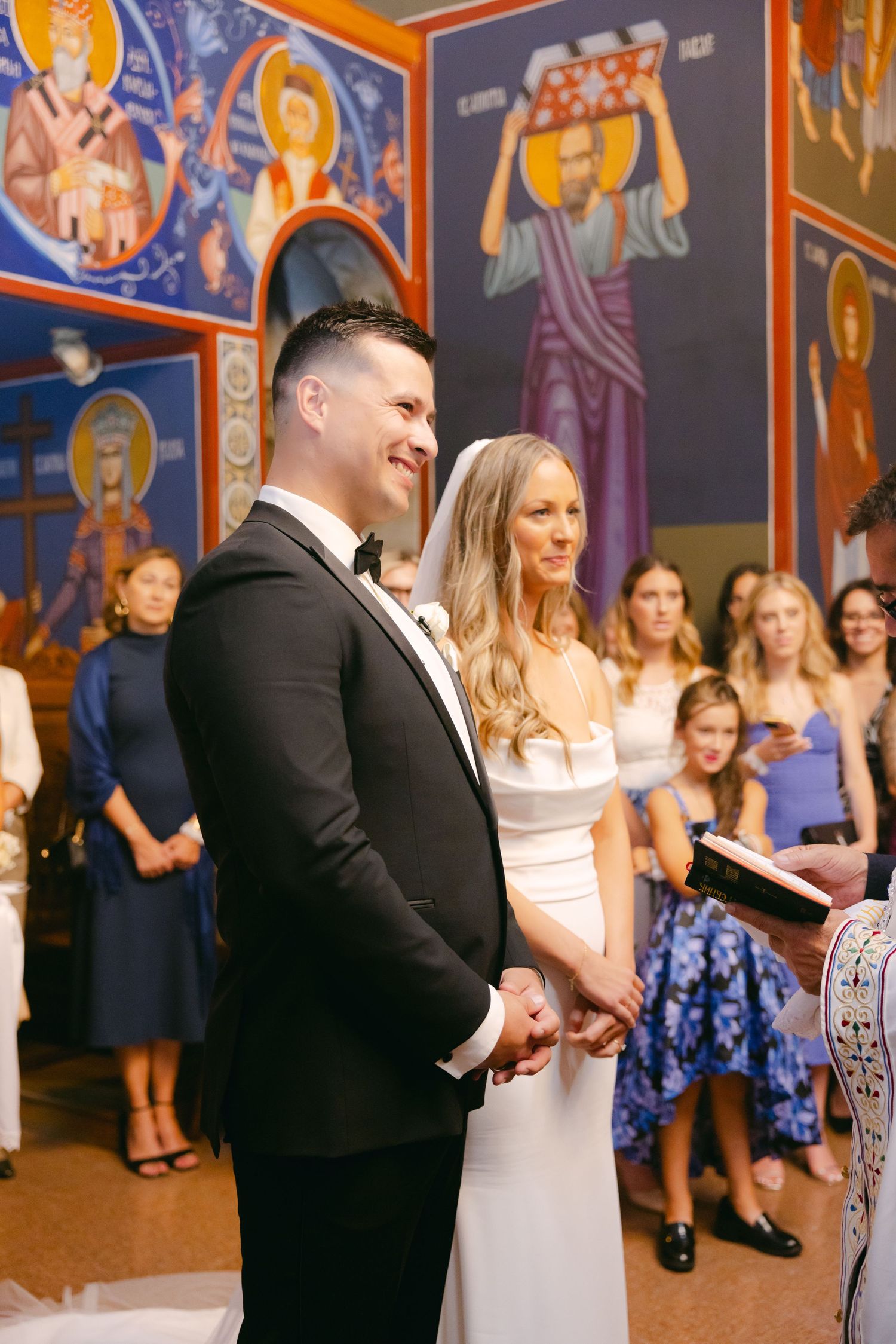 Orthodox wedding ceremony taking place in a church decorated with colorful religious murals and icons.