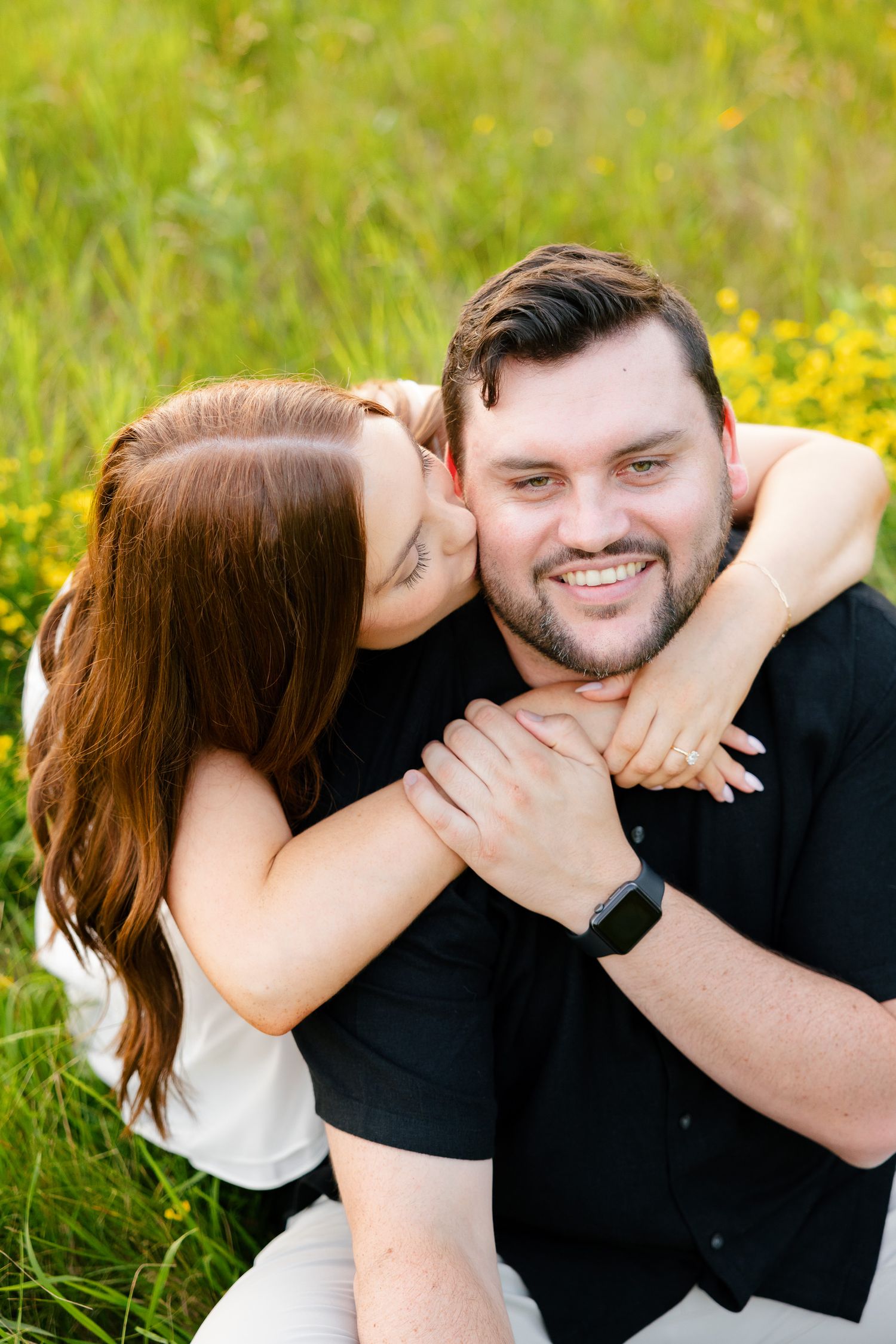 Sweet moment captured as couple embraces in sunny field with yellow wildflowers.