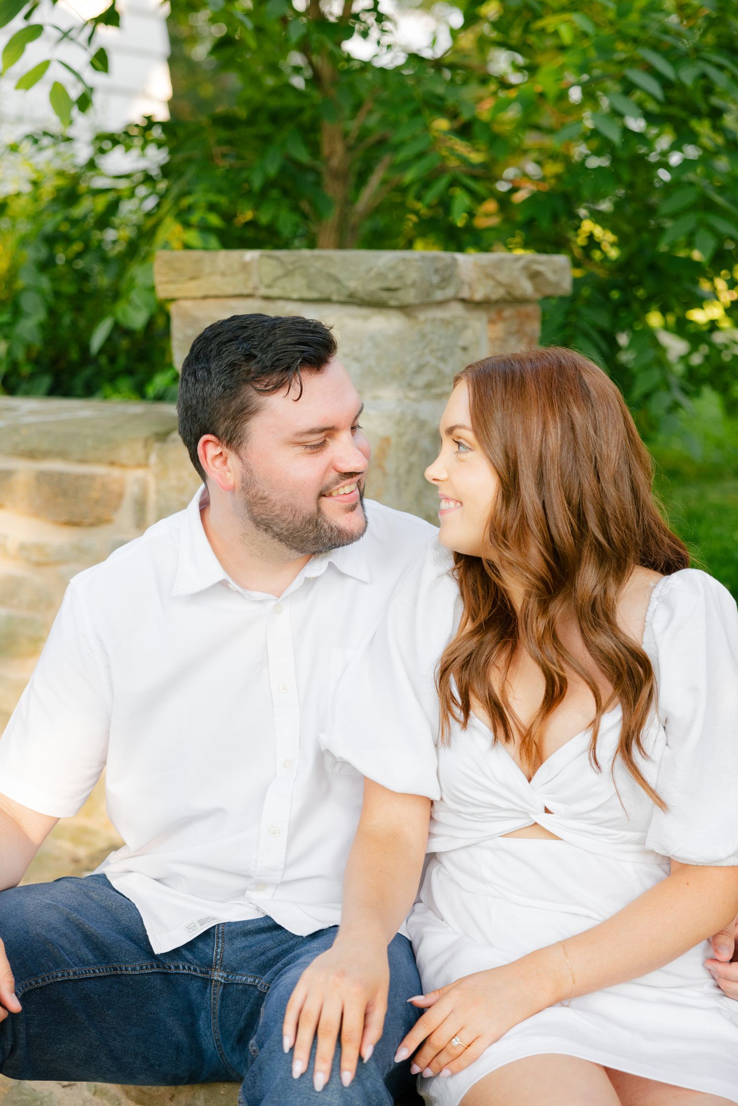Intimate portrait of couple in white clothing seated on stone steps exchanging loving glances.