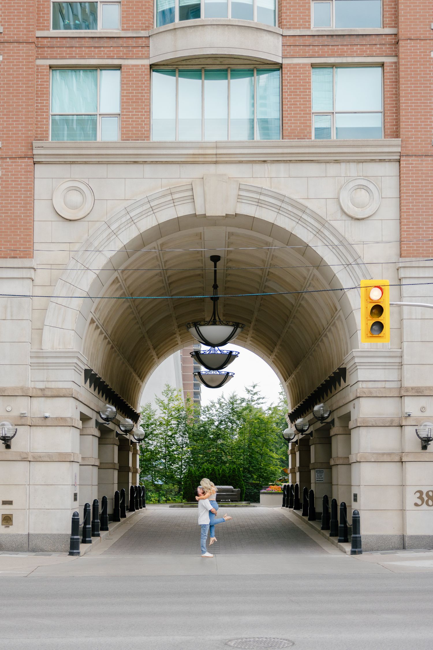 Person walking through arched brick tunnel with pendant lights overhead.