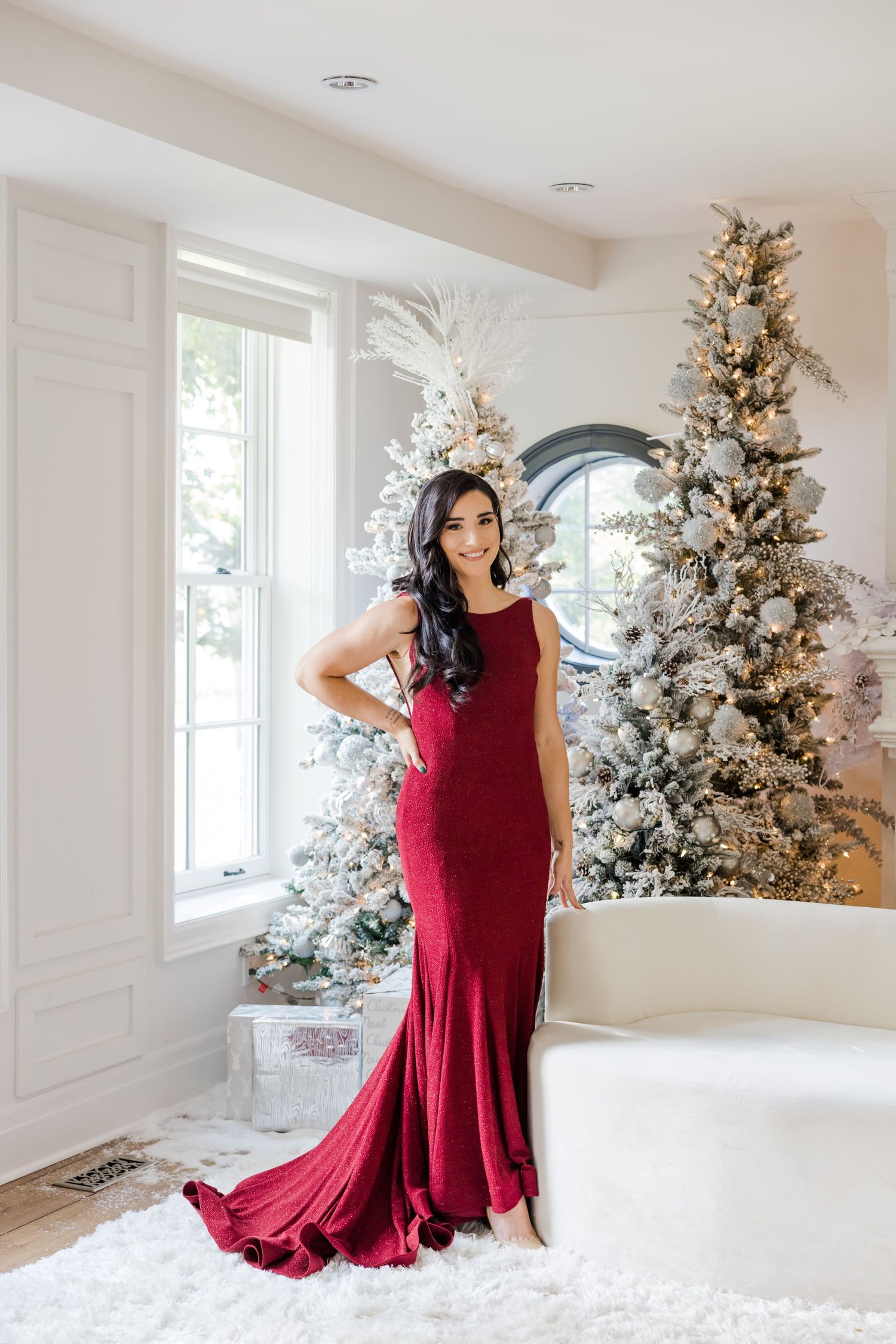 Formal portrait with crimson evening dress against white Christmas trees and holiday decorations.