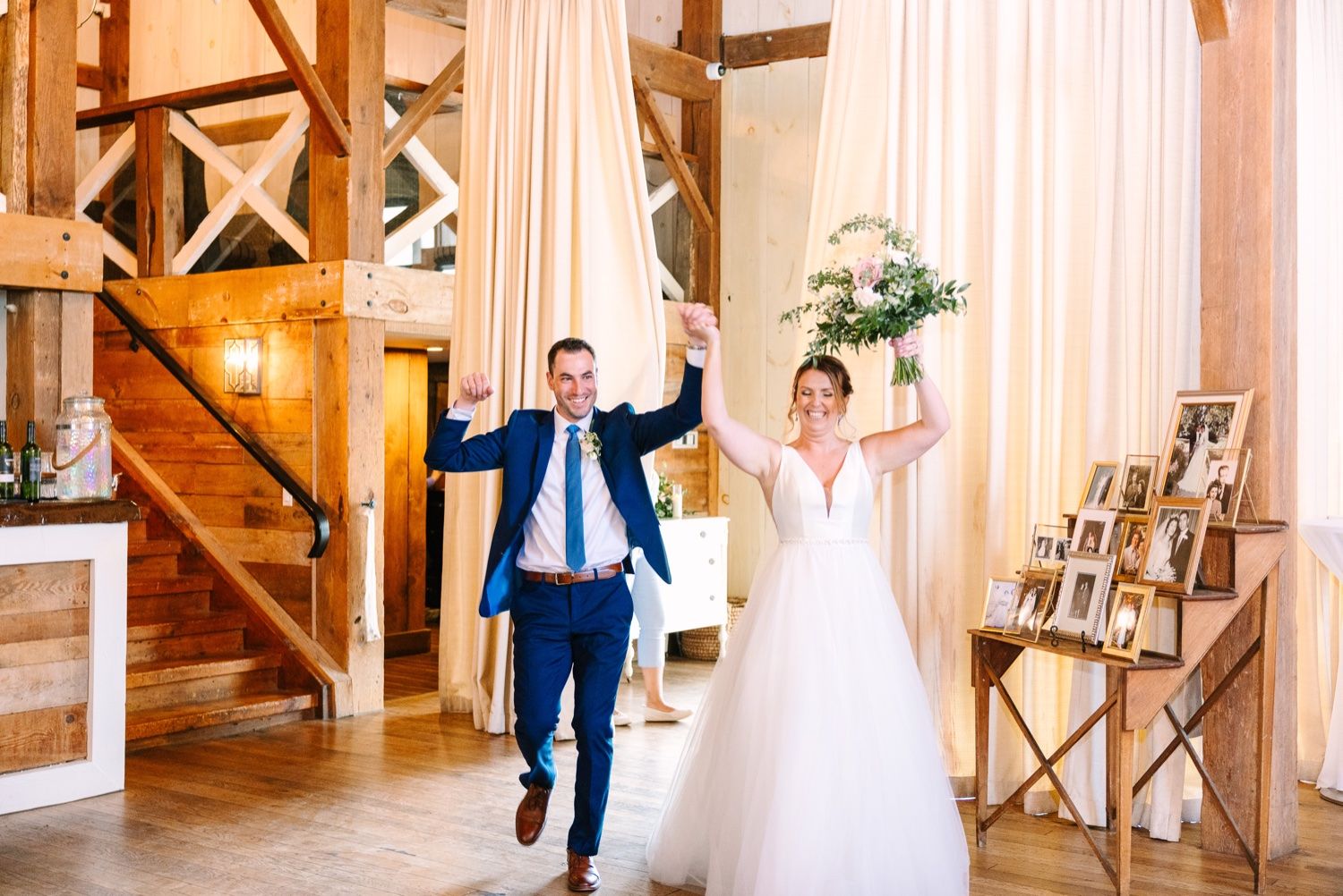Couple celebrates joyfully while walking down the aisle in a rustic barn venue with flowing drapes and wooden beams.