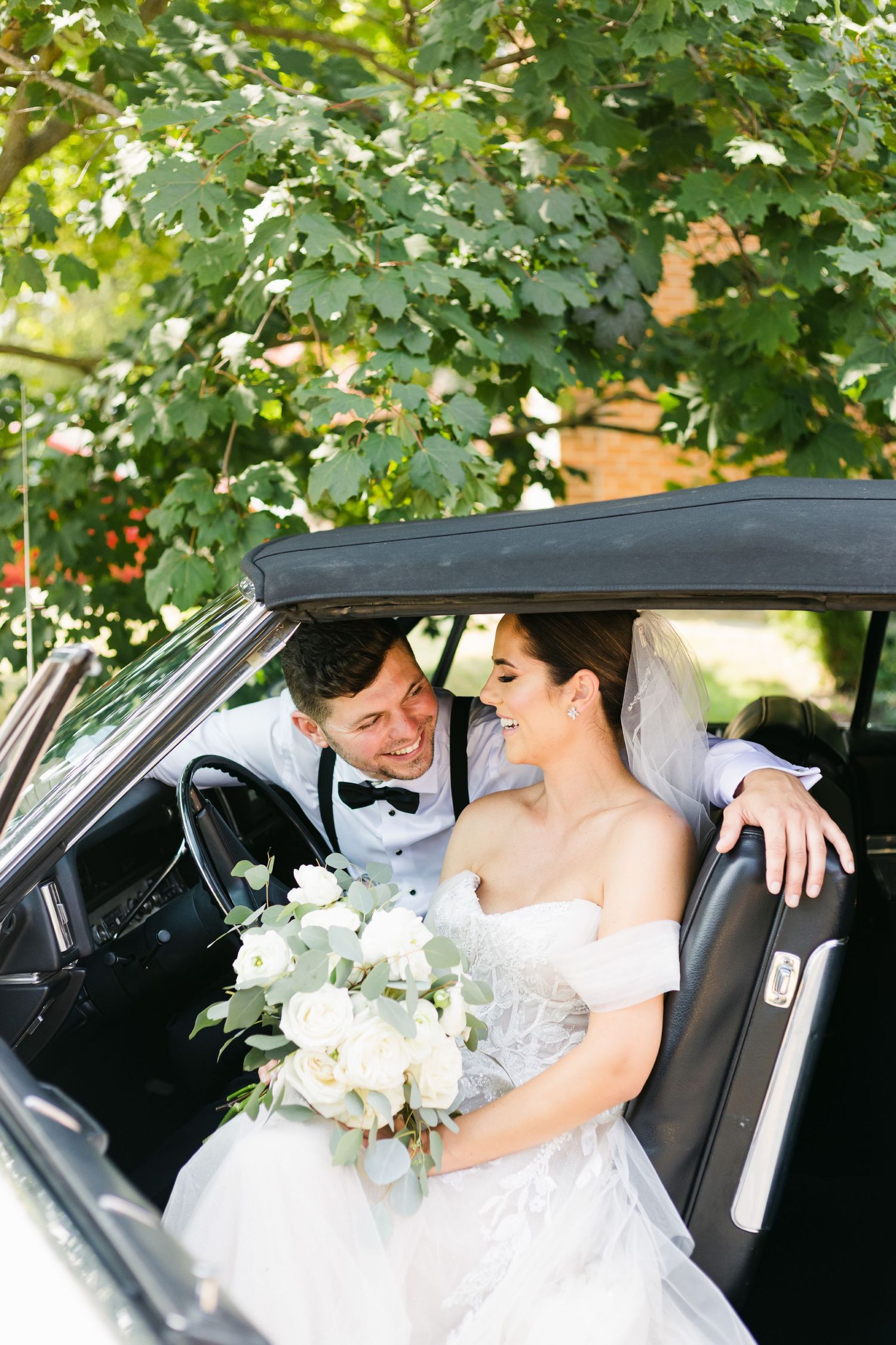 Romantic wedding moment captured inside vintage car with white floral bouquet.