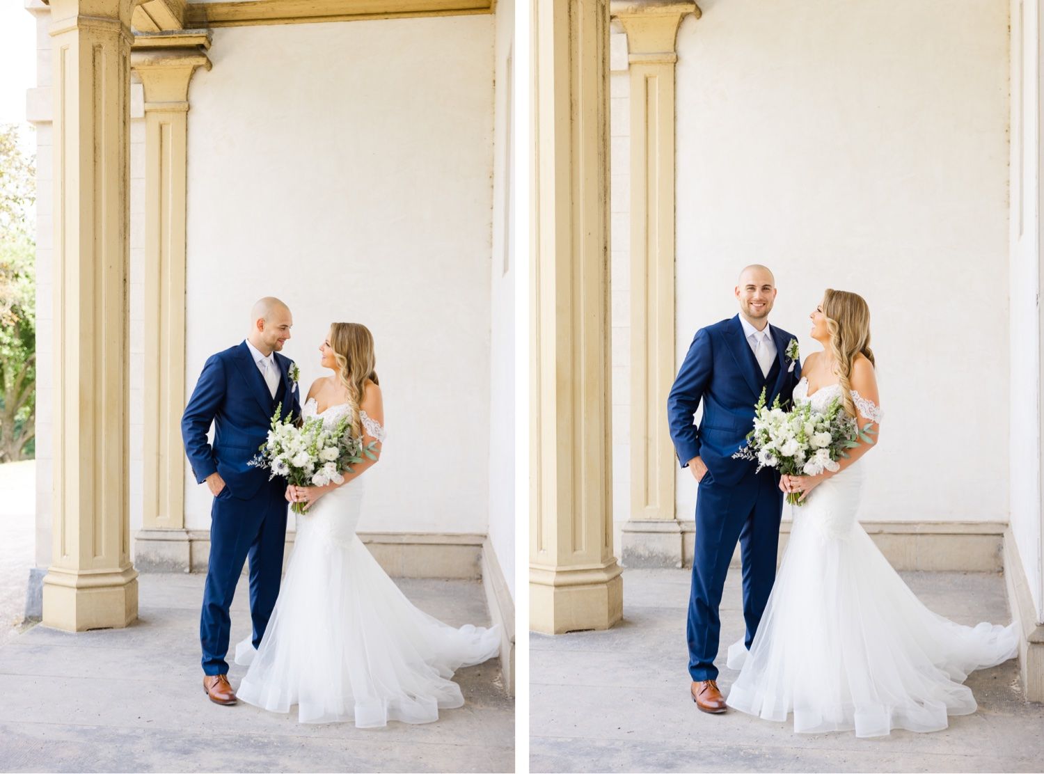 A romantic wedding couple poses in front of elegant white columns wearing a navy suit and flowing white gown.