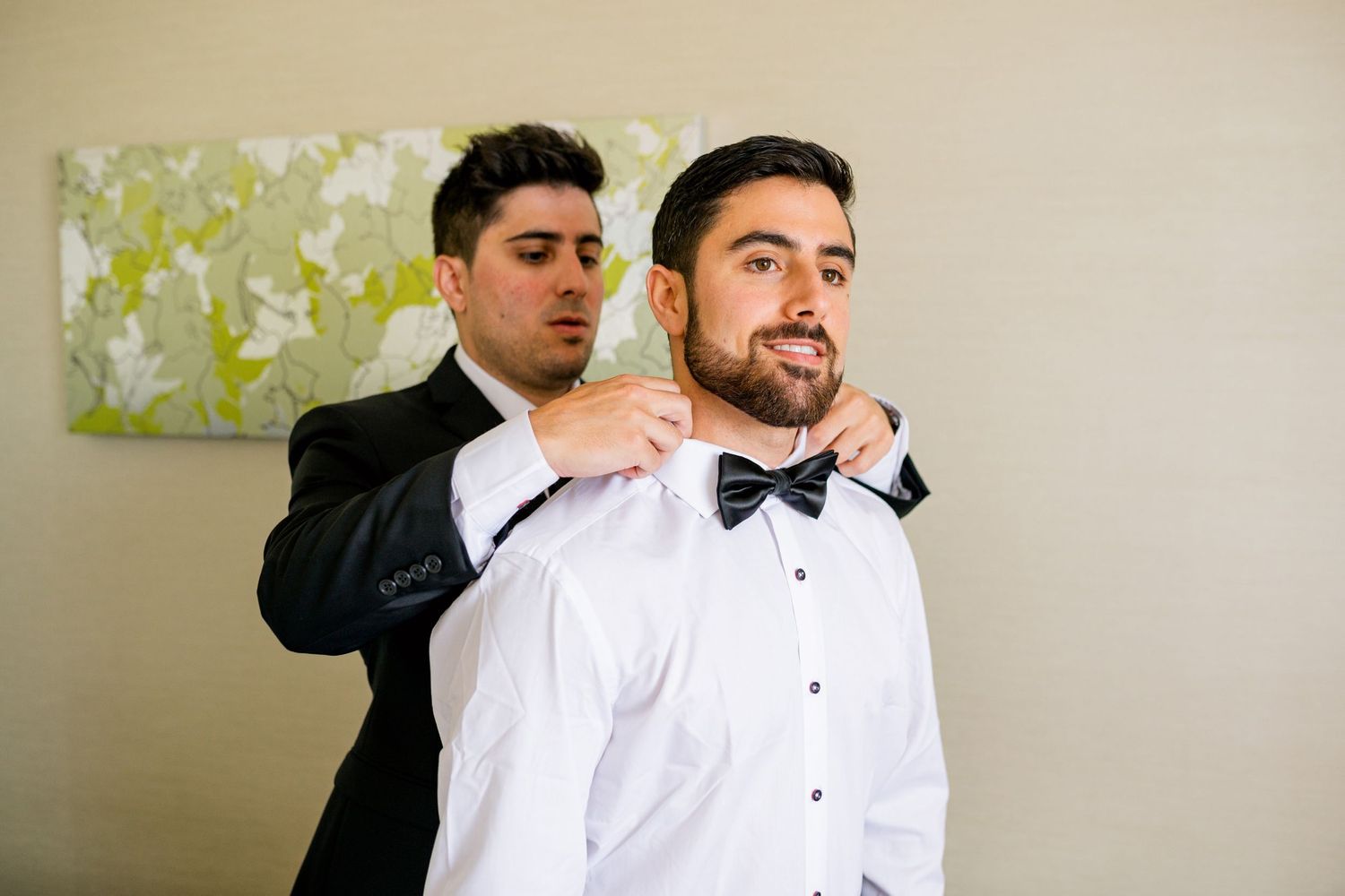 Two people adjusting formal attire and bow ties before wedding ceremony.