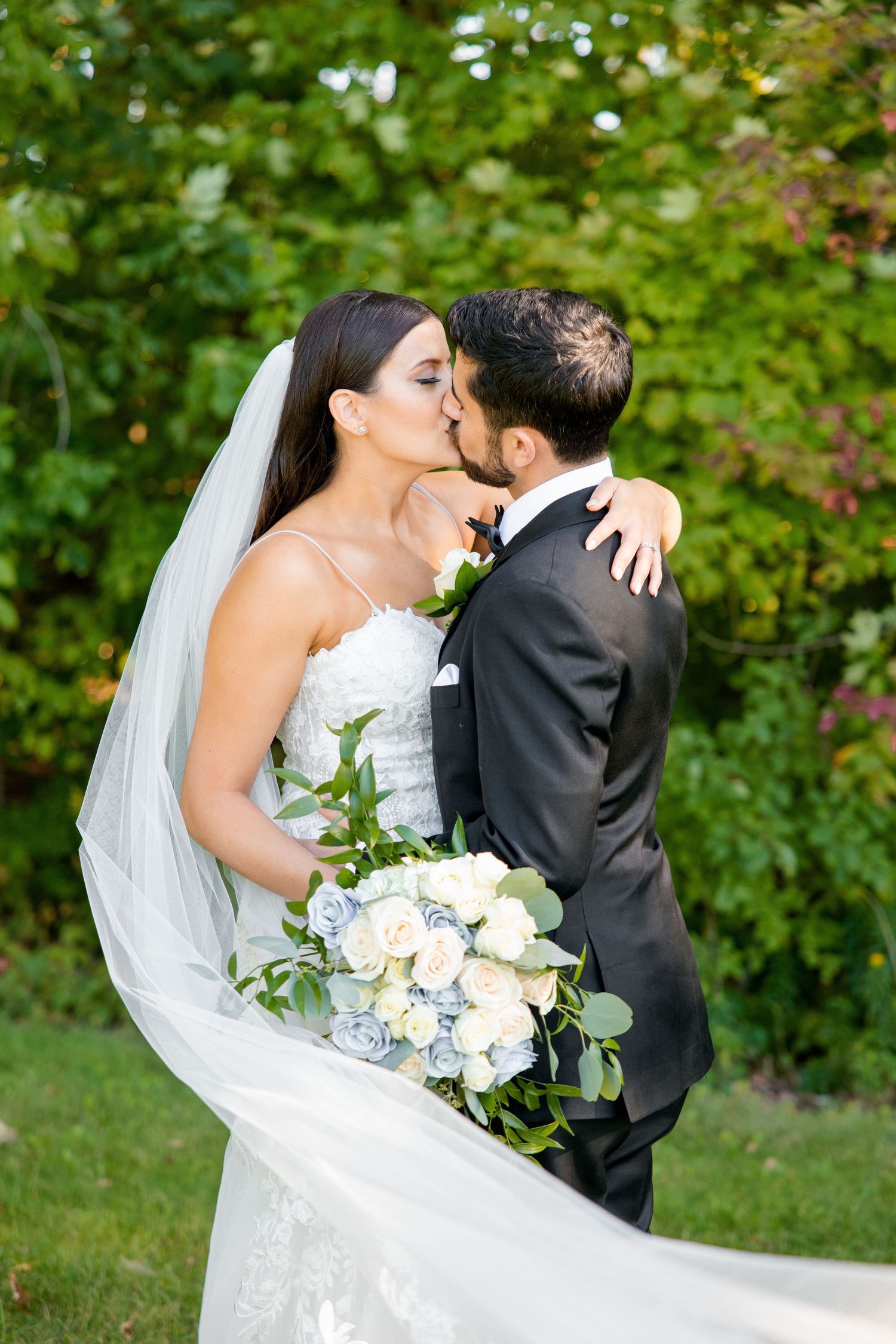 Outdoor wedding portrait captures intimate moment with flowing veil and white rose bouquet.