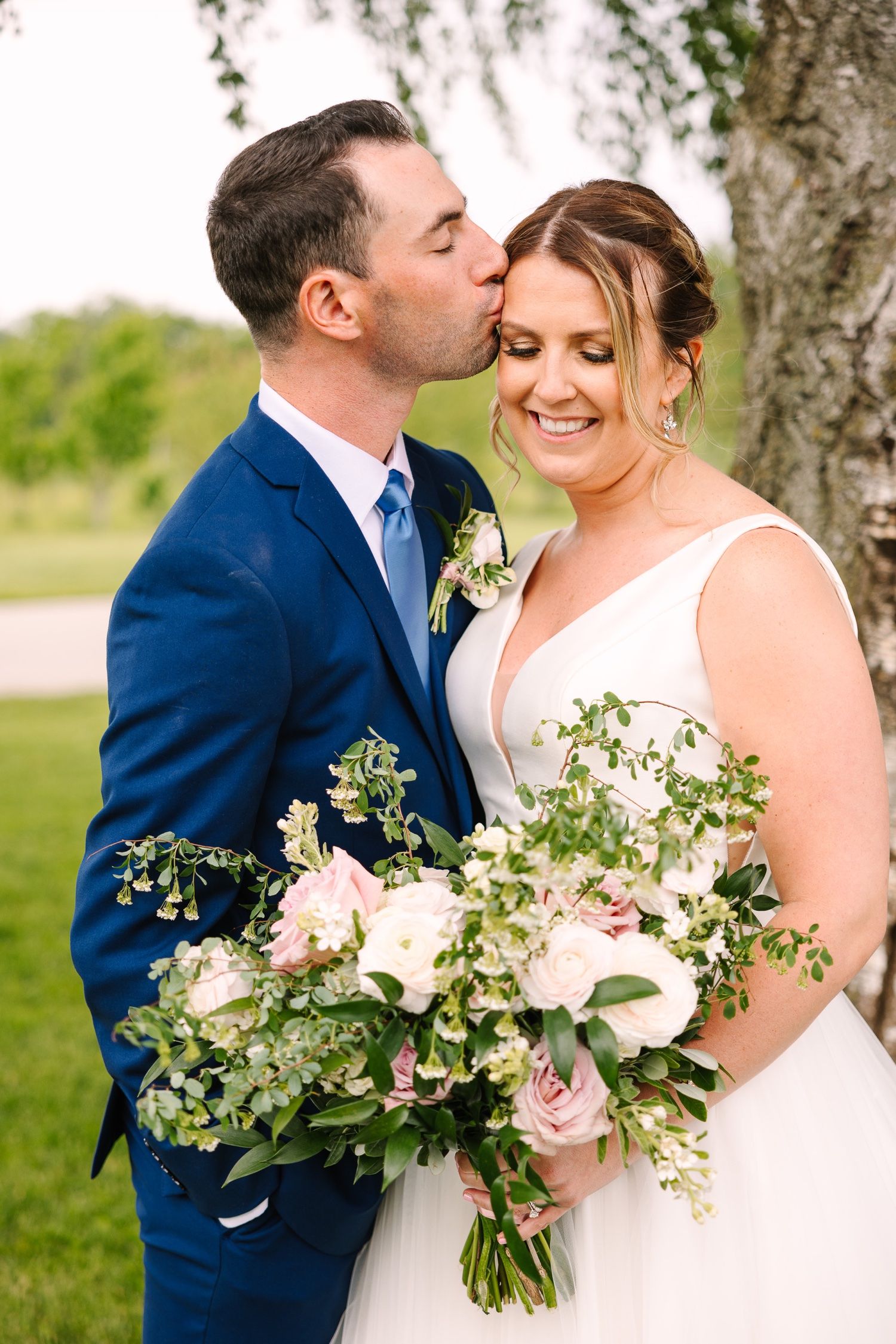 Intimate wedding portrait with elegant white and blush floral bouquet under tree.